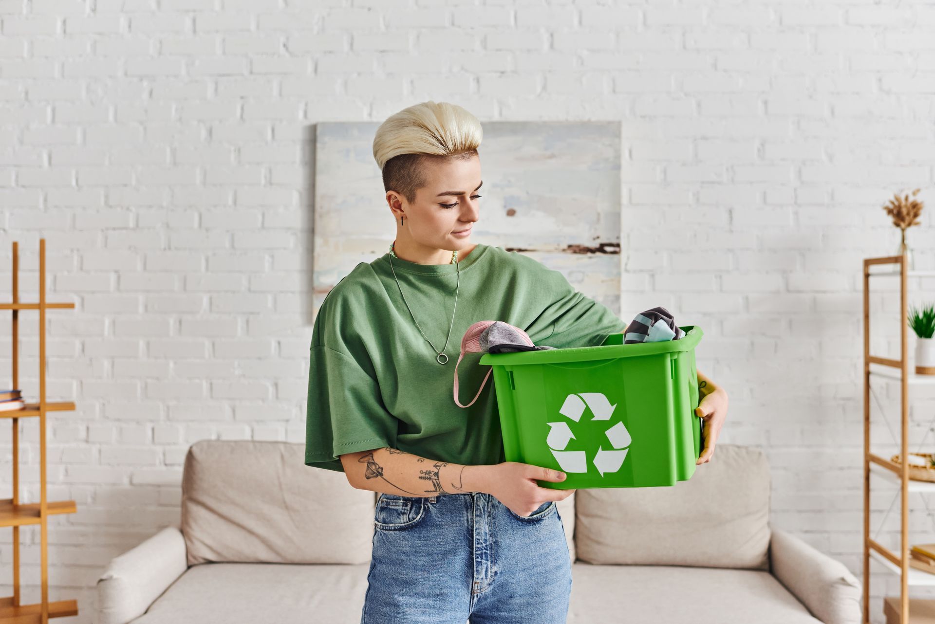 A woman is holding a green recycling bin in her living room.