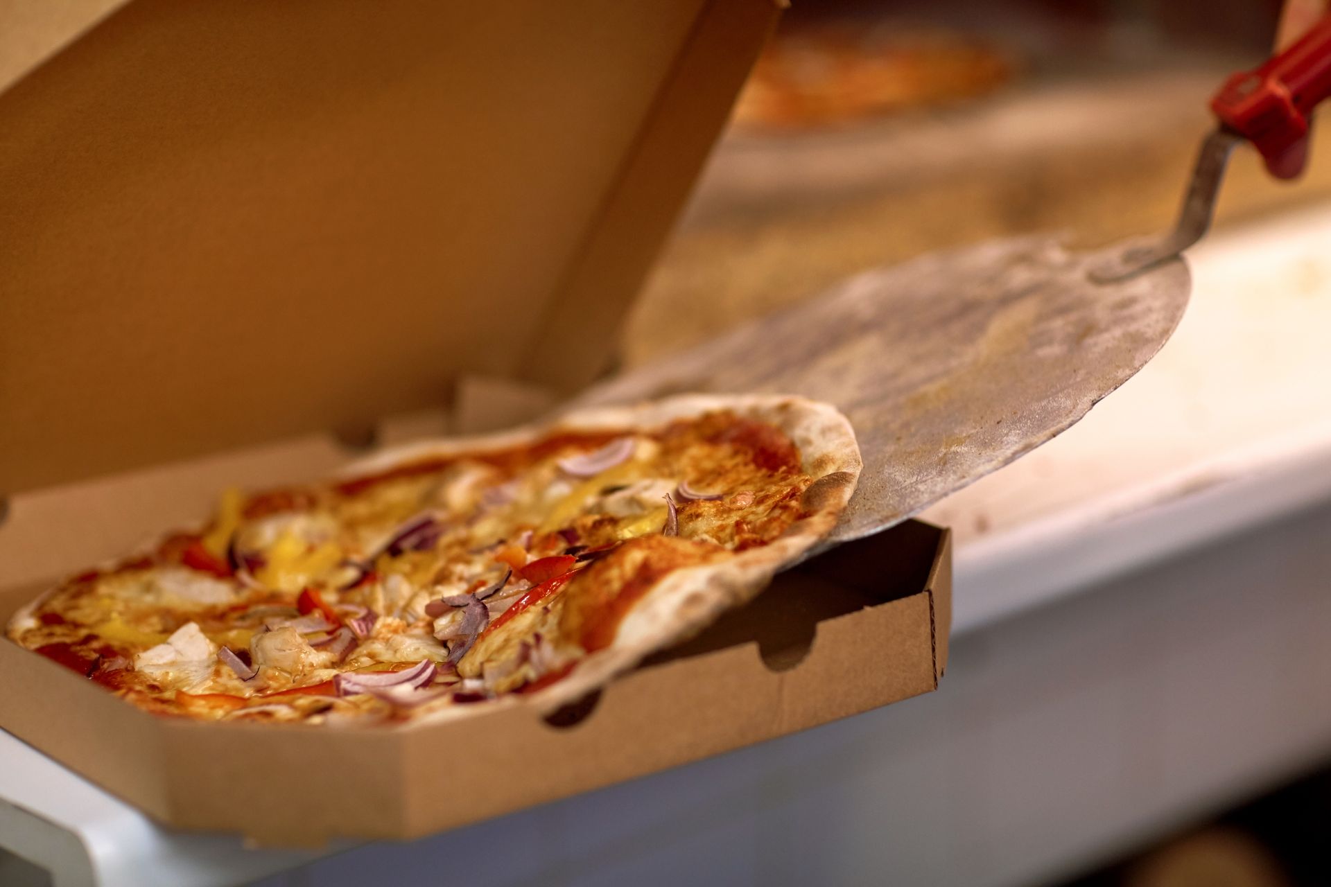 Pizza being placed in a cardboard box with a pizza peel, indoors. — Romanas Italian Restaurant in Nobby Beach, QLD