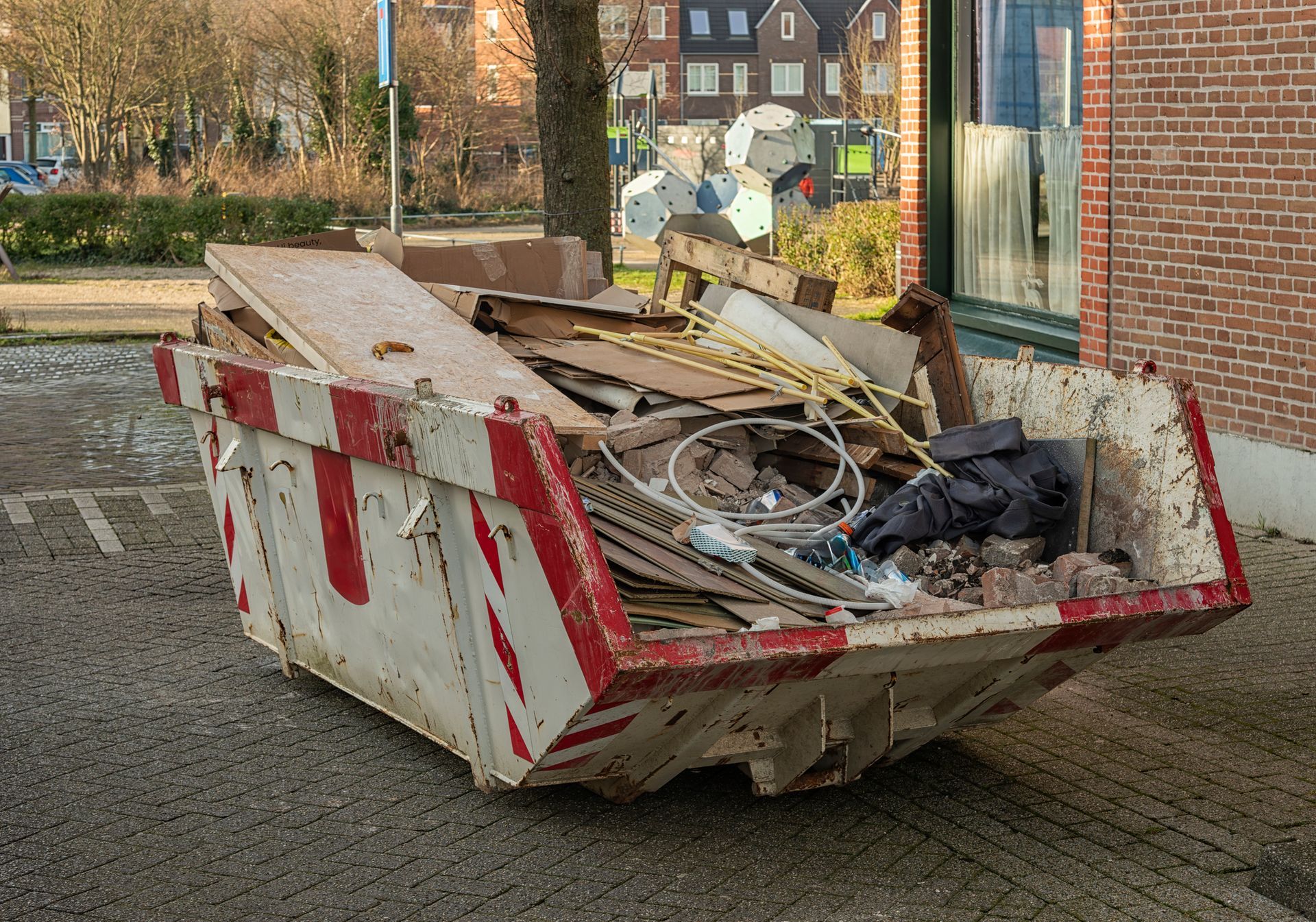 White and red striped dumpster overflowing with construction debris on a paved surface.