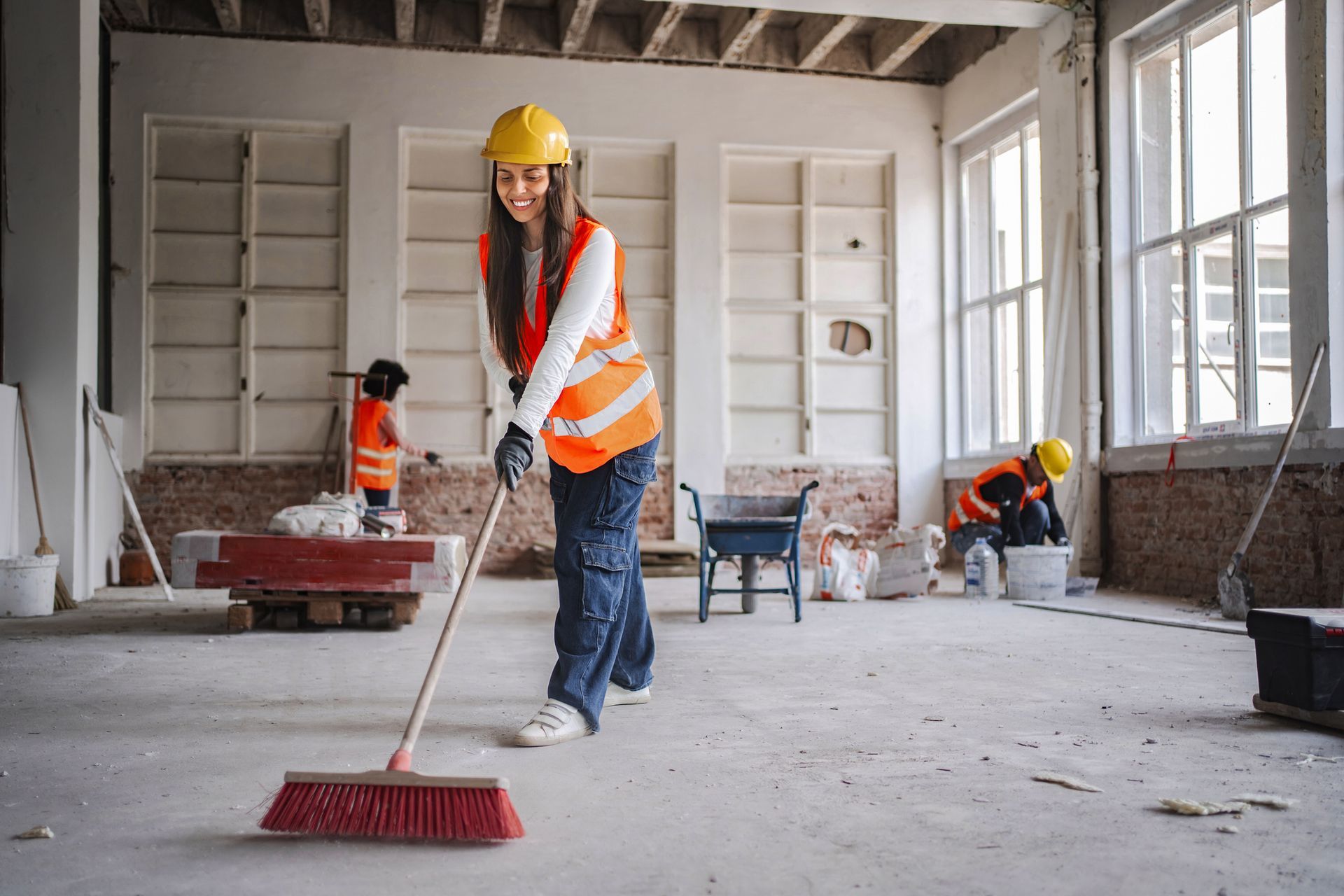 Woman in safety gear sweeping construction site floor.
