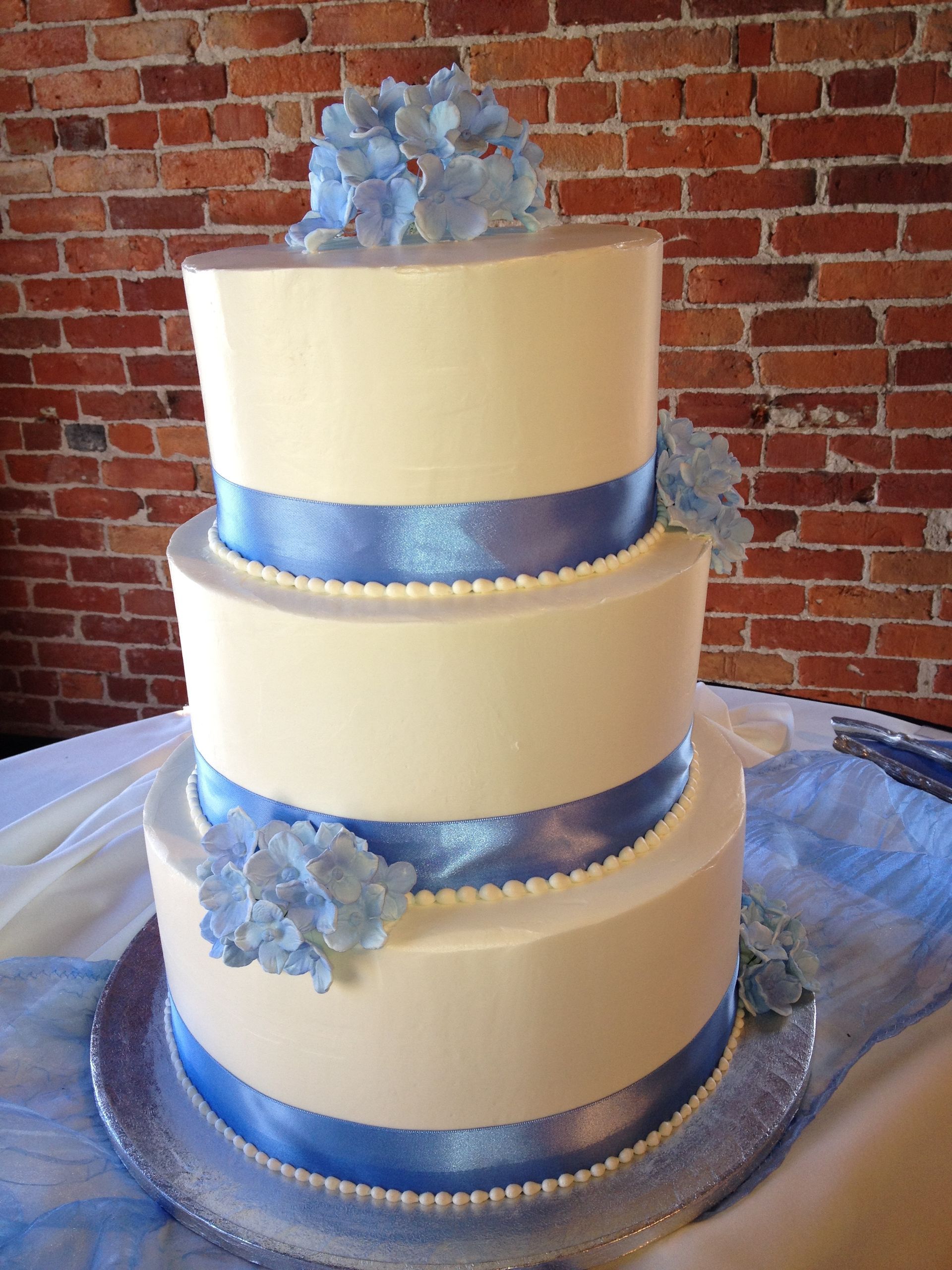 a white wedding cake with blue ribbon and flowers