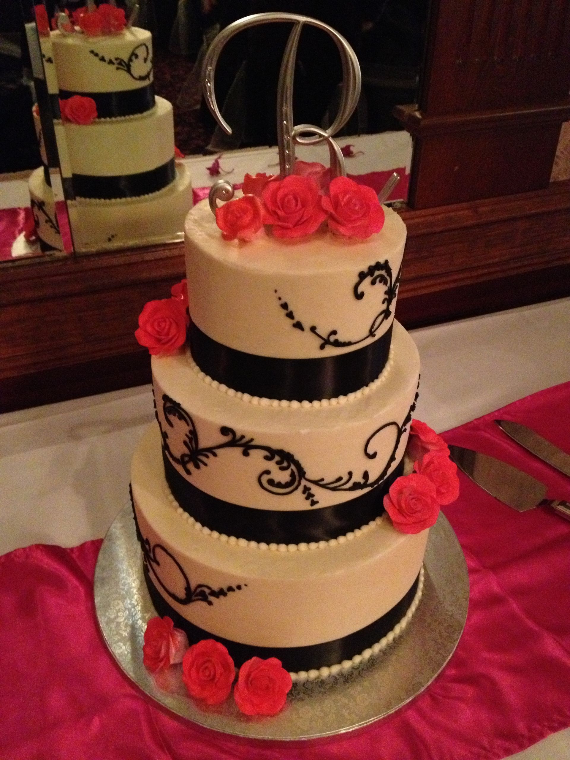 a black and white wedding cake with red roses and a letter p on top