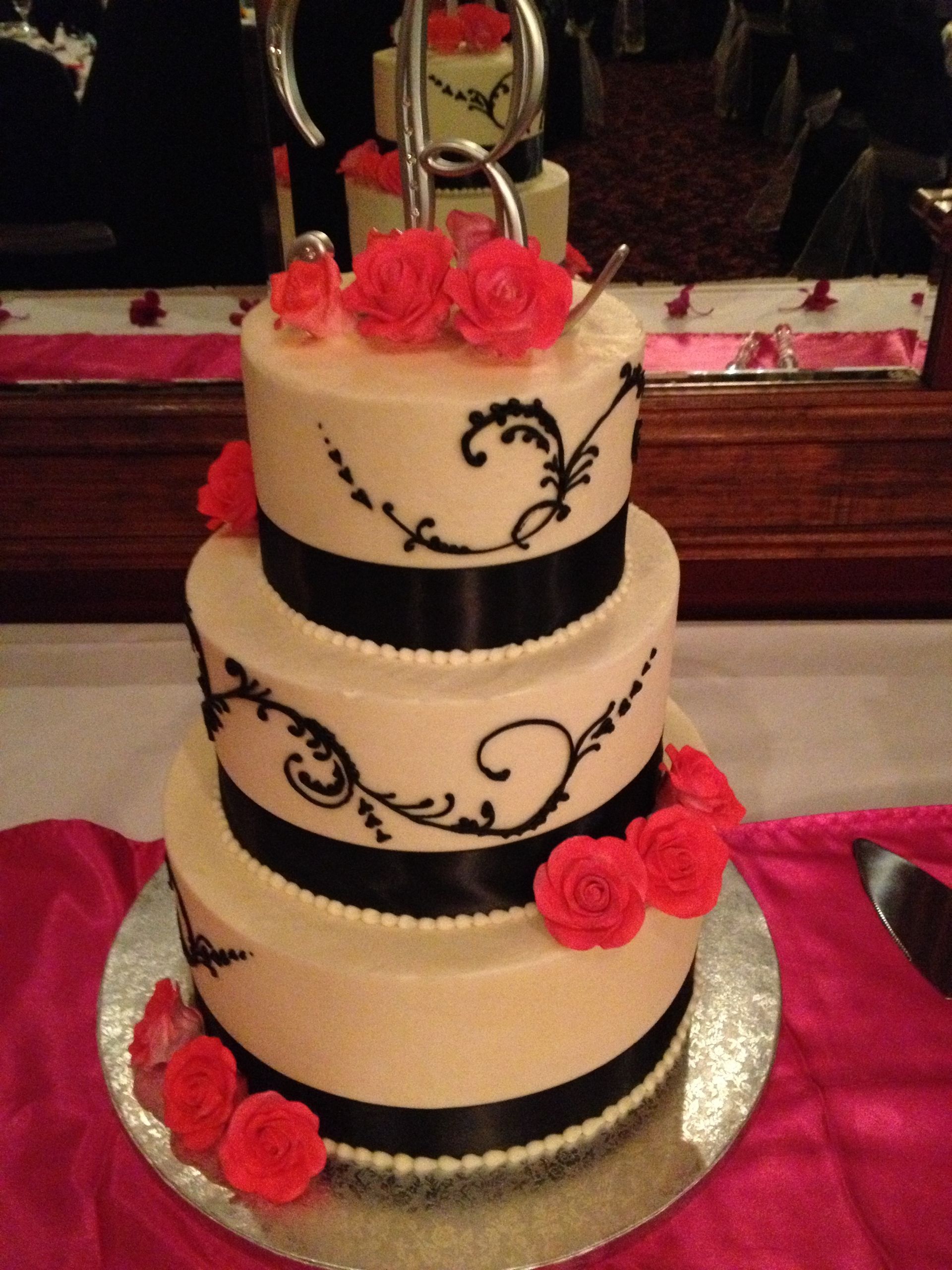 a three tiered cake with red roses and black ribbons