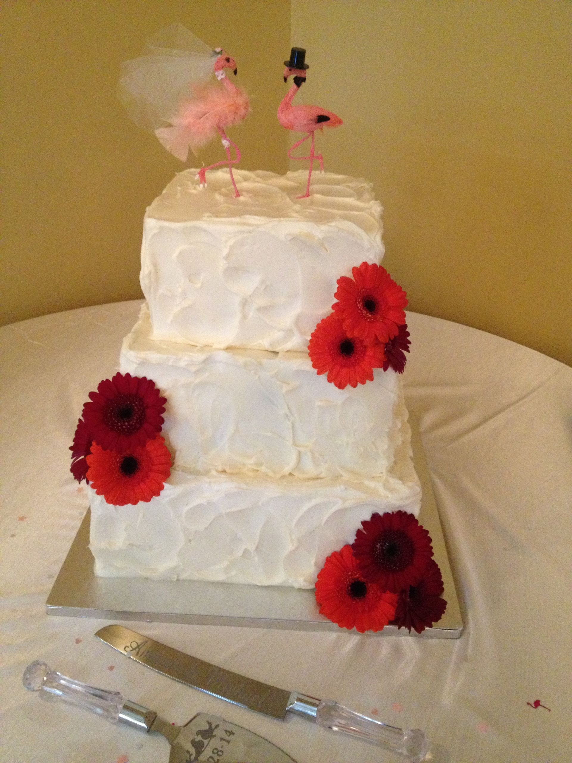 a wedding cake with flamingos on top and red flowers
