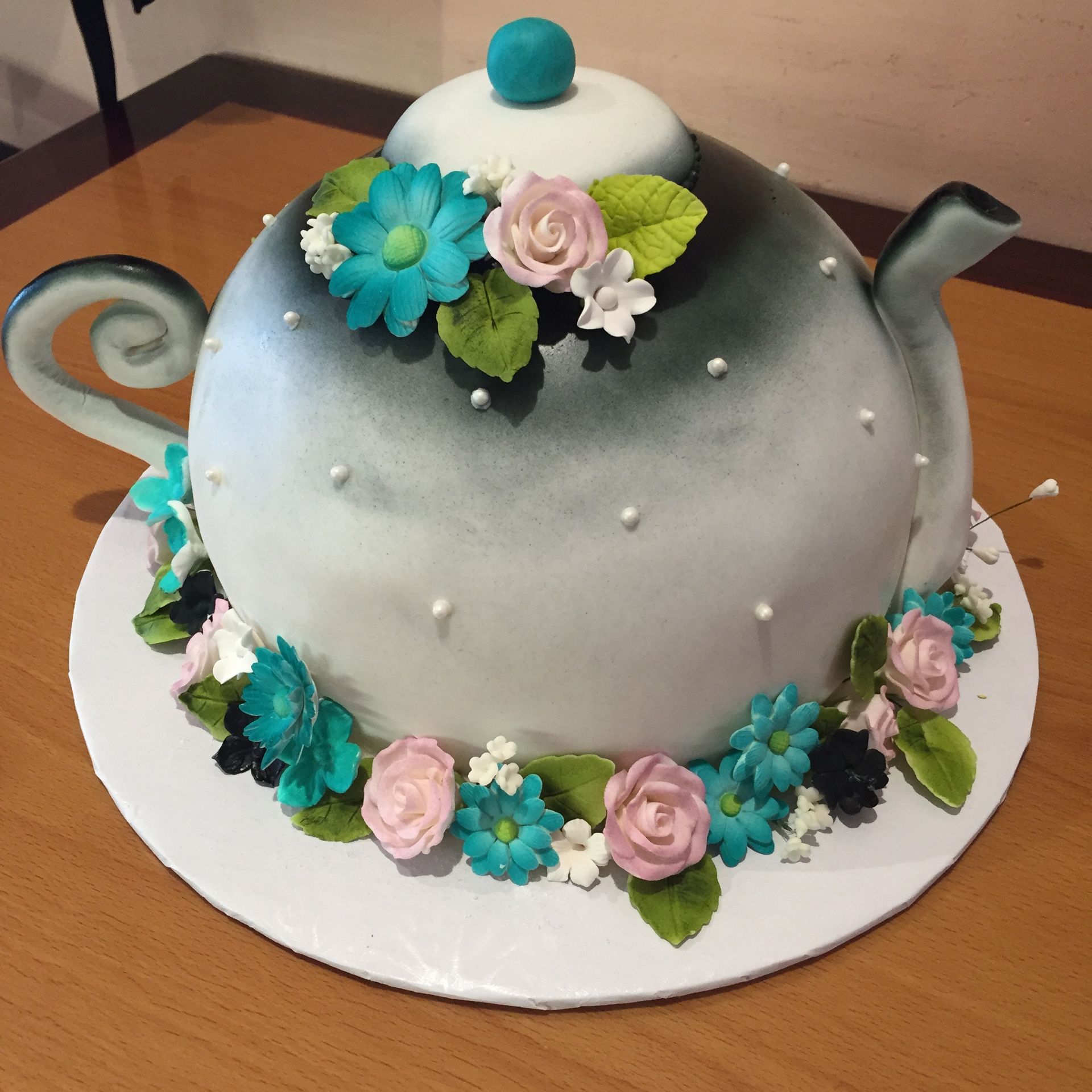 a cake in the shape of a teapot decorated with flowers and pearls