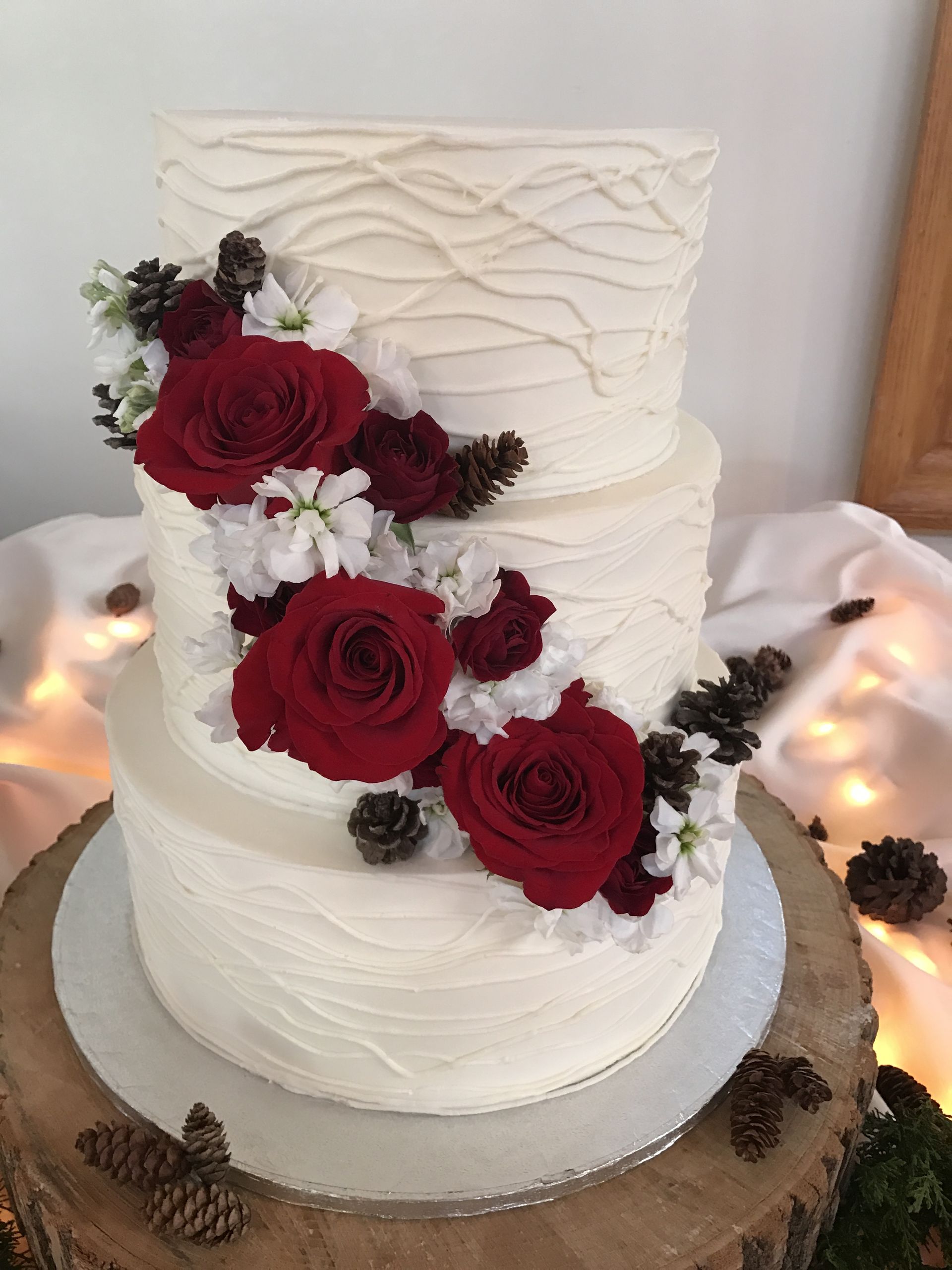 a white wedding cake with red roses and pine cones on top .