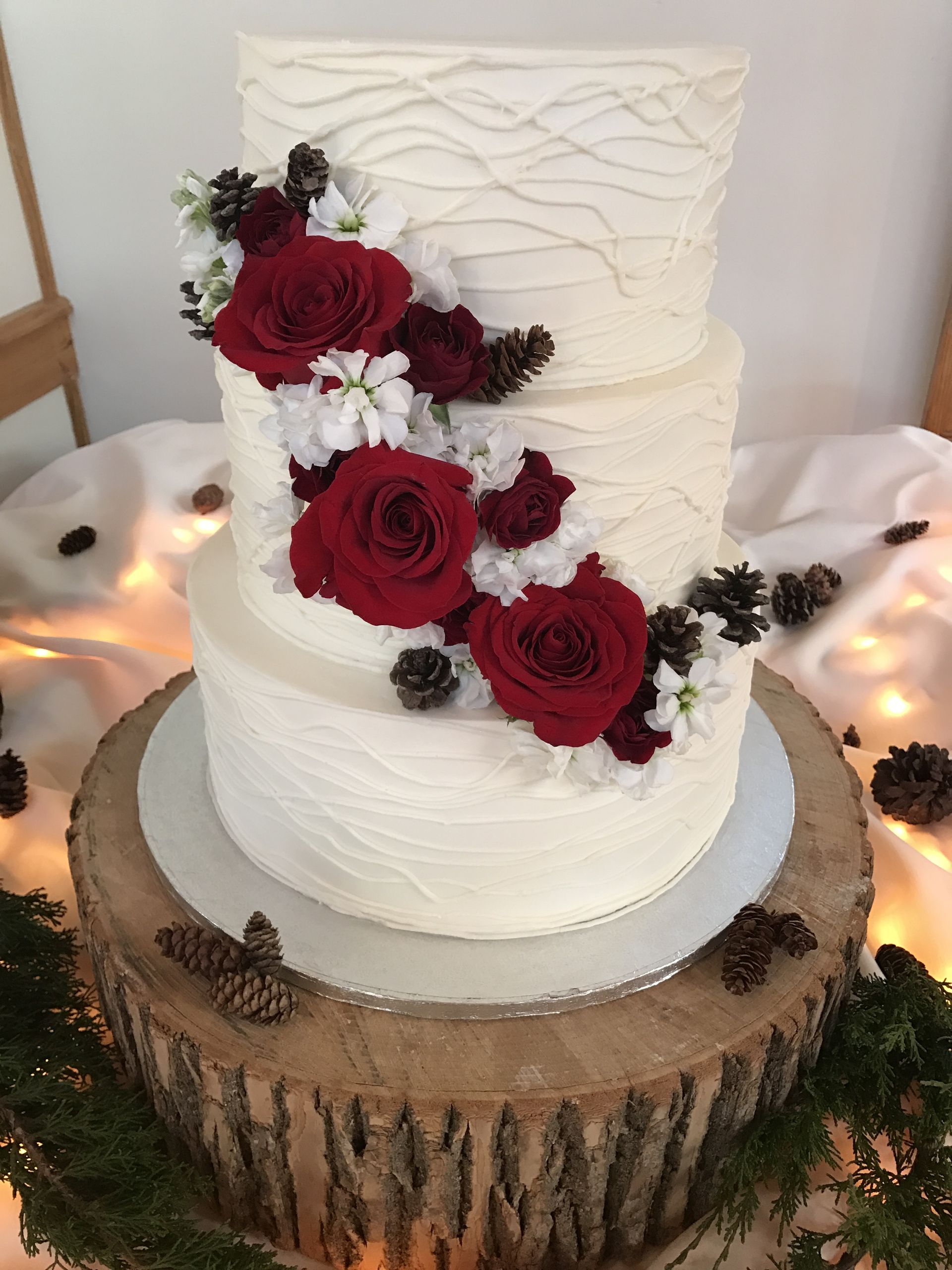 a white wedding cake with red roses and pine cones on a wooden stump .