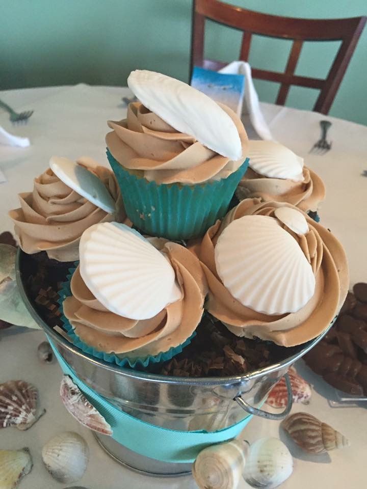 a bucket filled with cupcakes decorated with seashells on a table .
