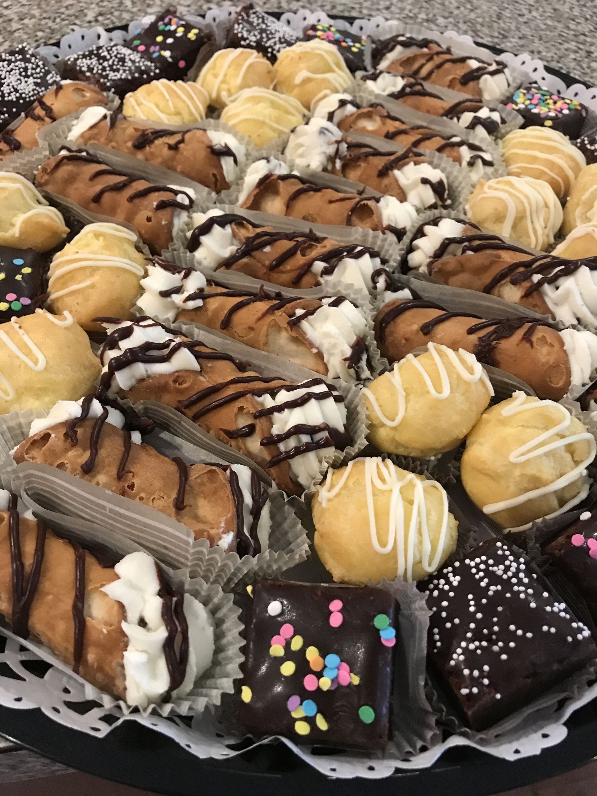 a tray filled with a variety of desserts including cannoli and cupcakes