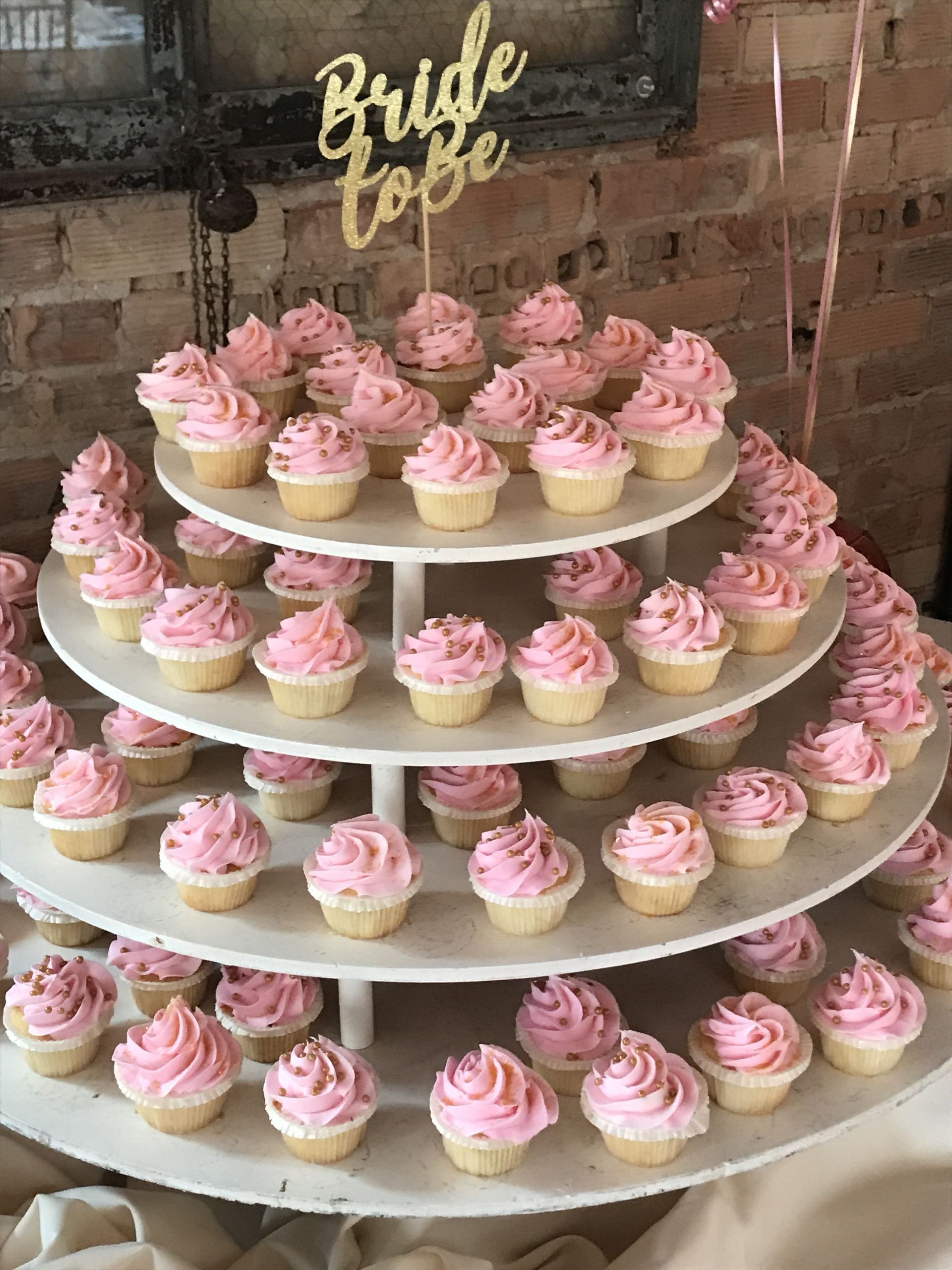 a cupcake tower filled with pink frosted cupcakes for a bridal shower .