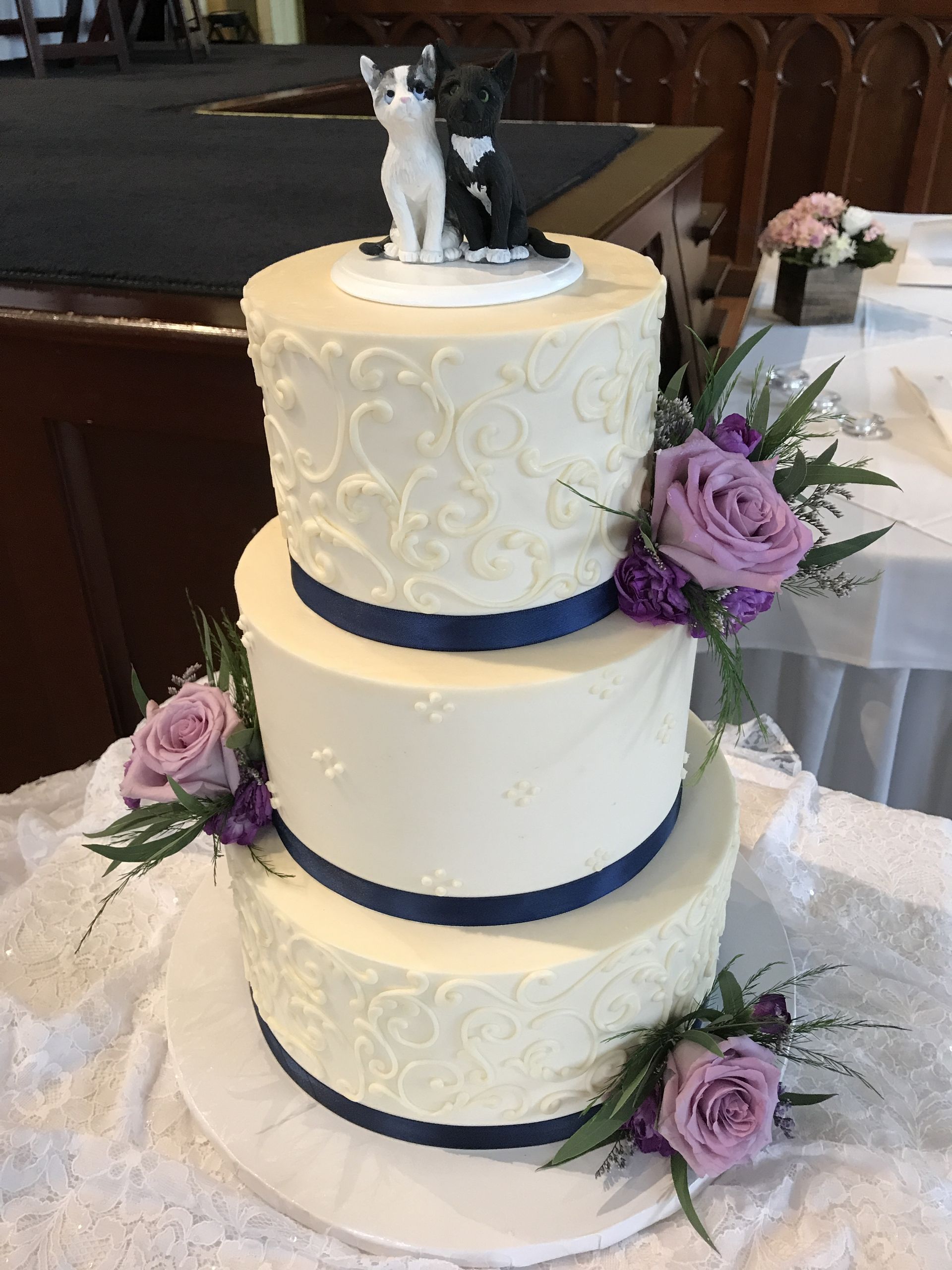 a wedding cake with purple roses and a cat on top
