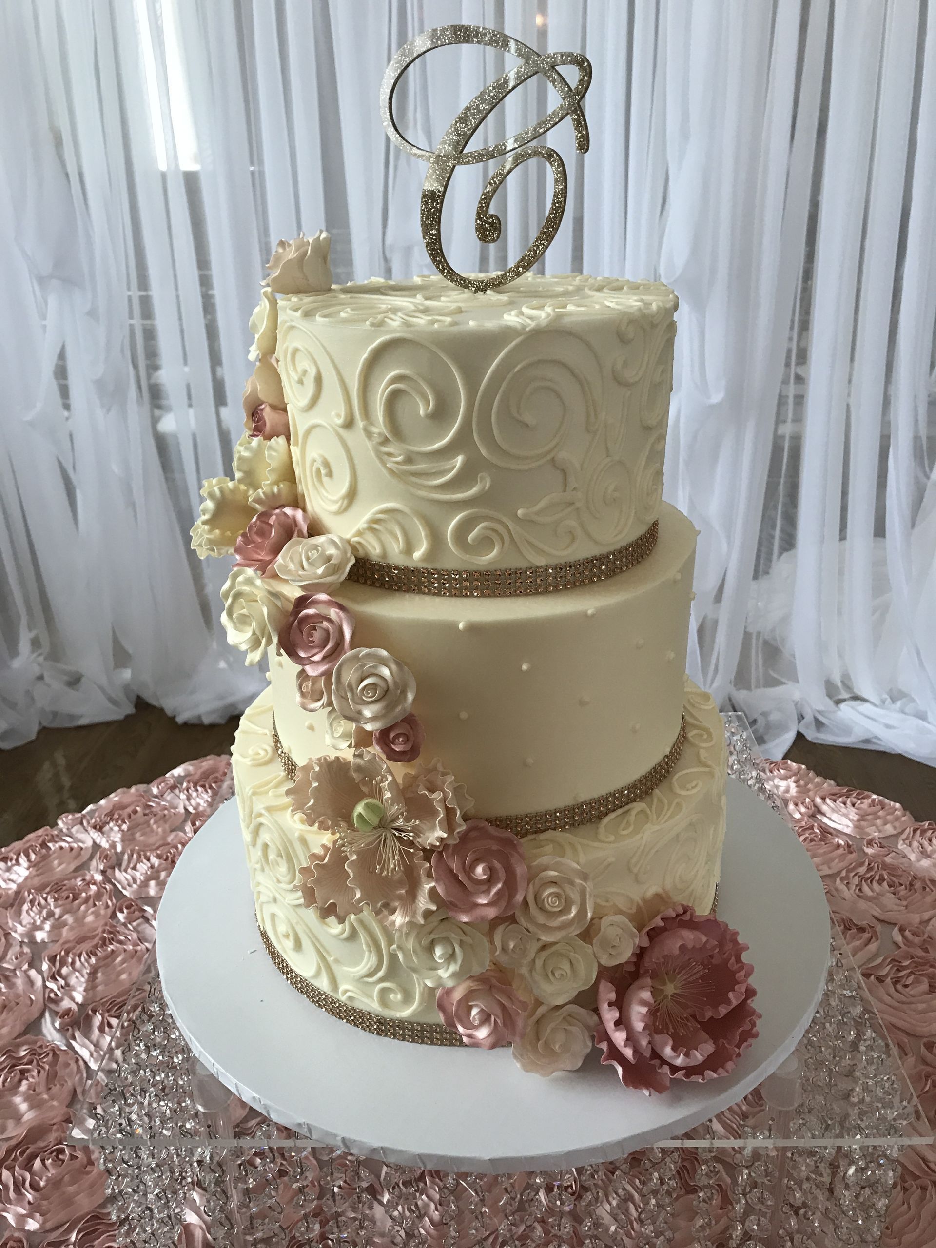 a three tiered wedding cake with flowers and a monogram on top is sitting on a table .