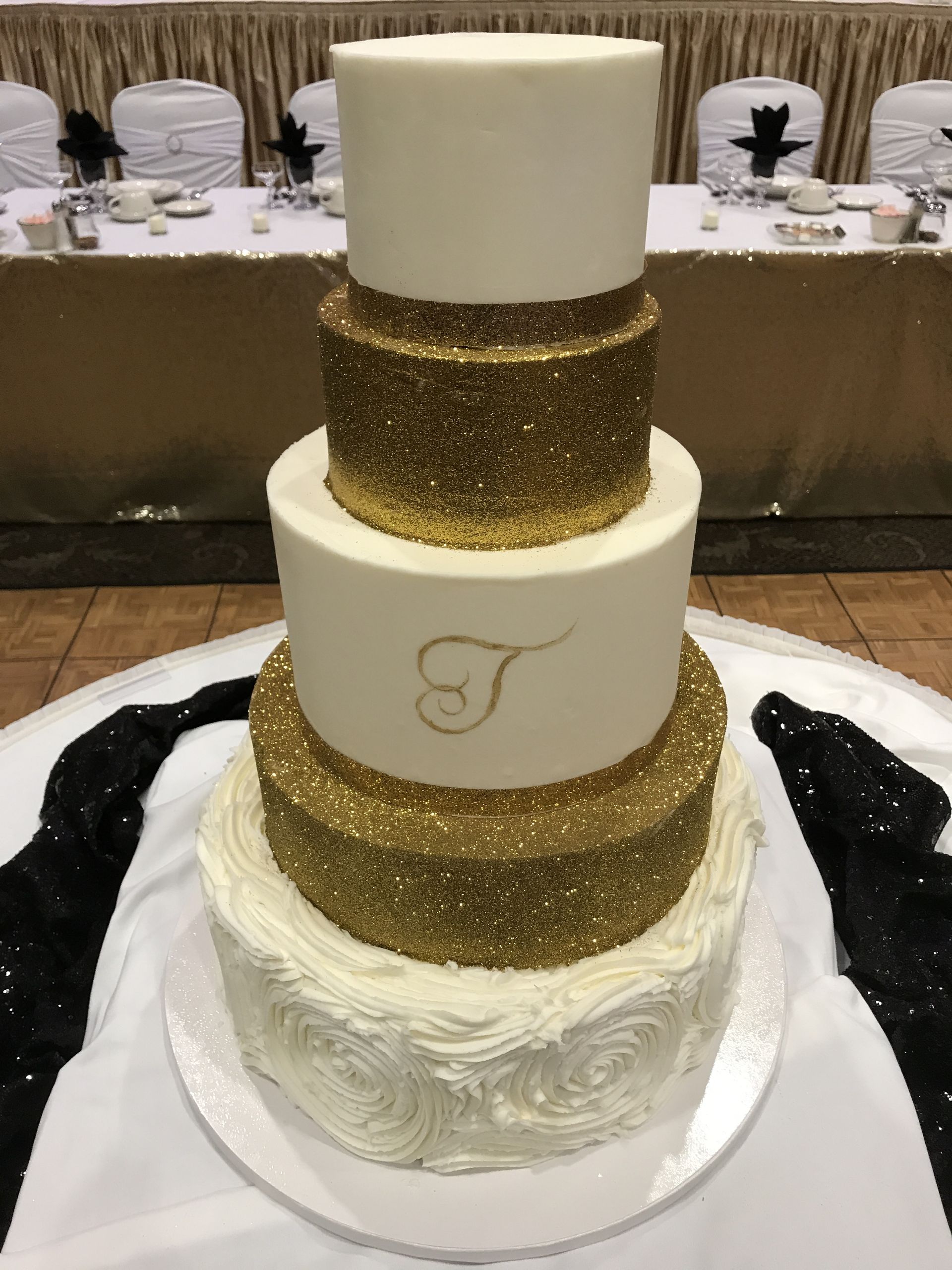 a white and gold wedding cake with the letter t on it