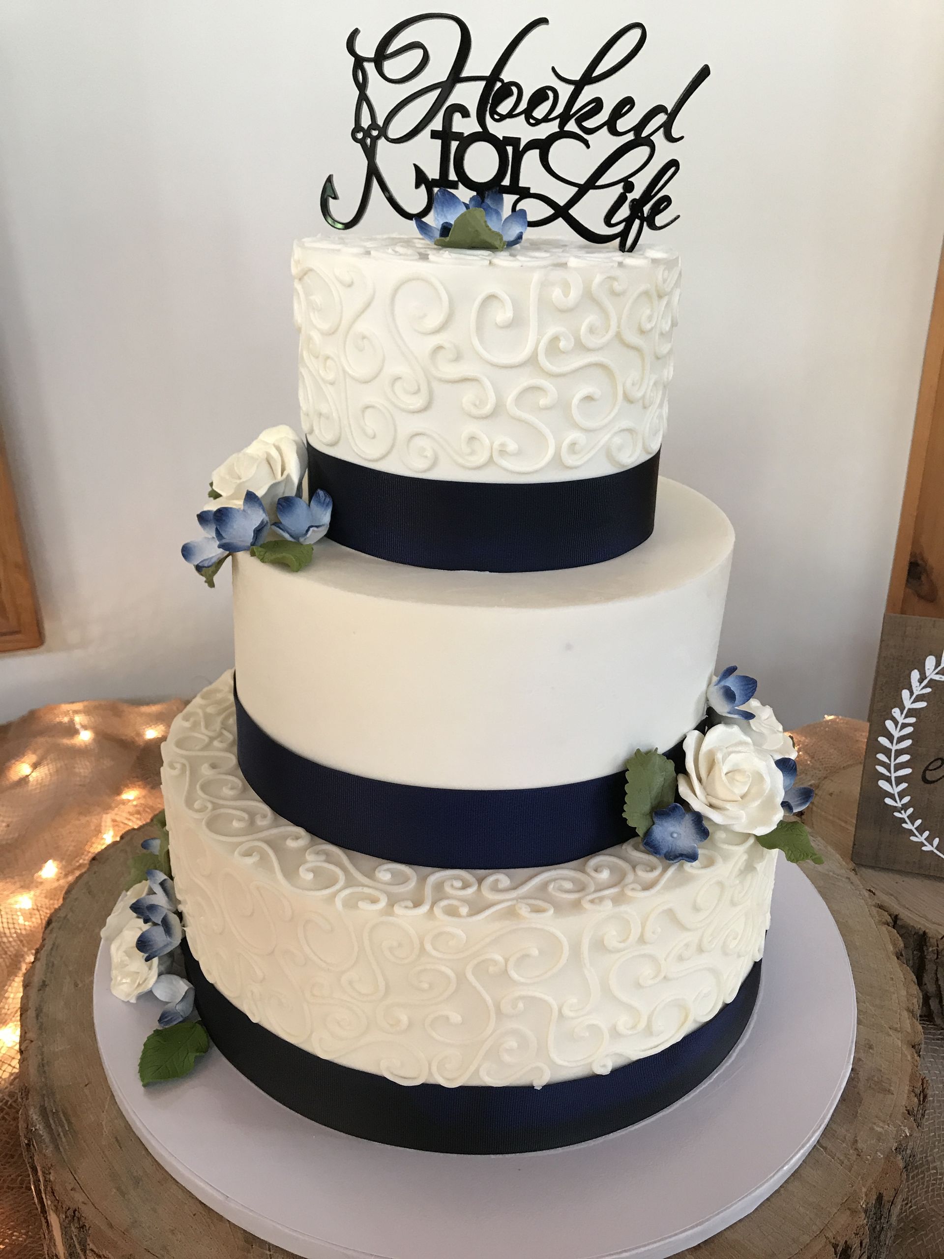a white and blue wedding cake with a topper that says hooked for life