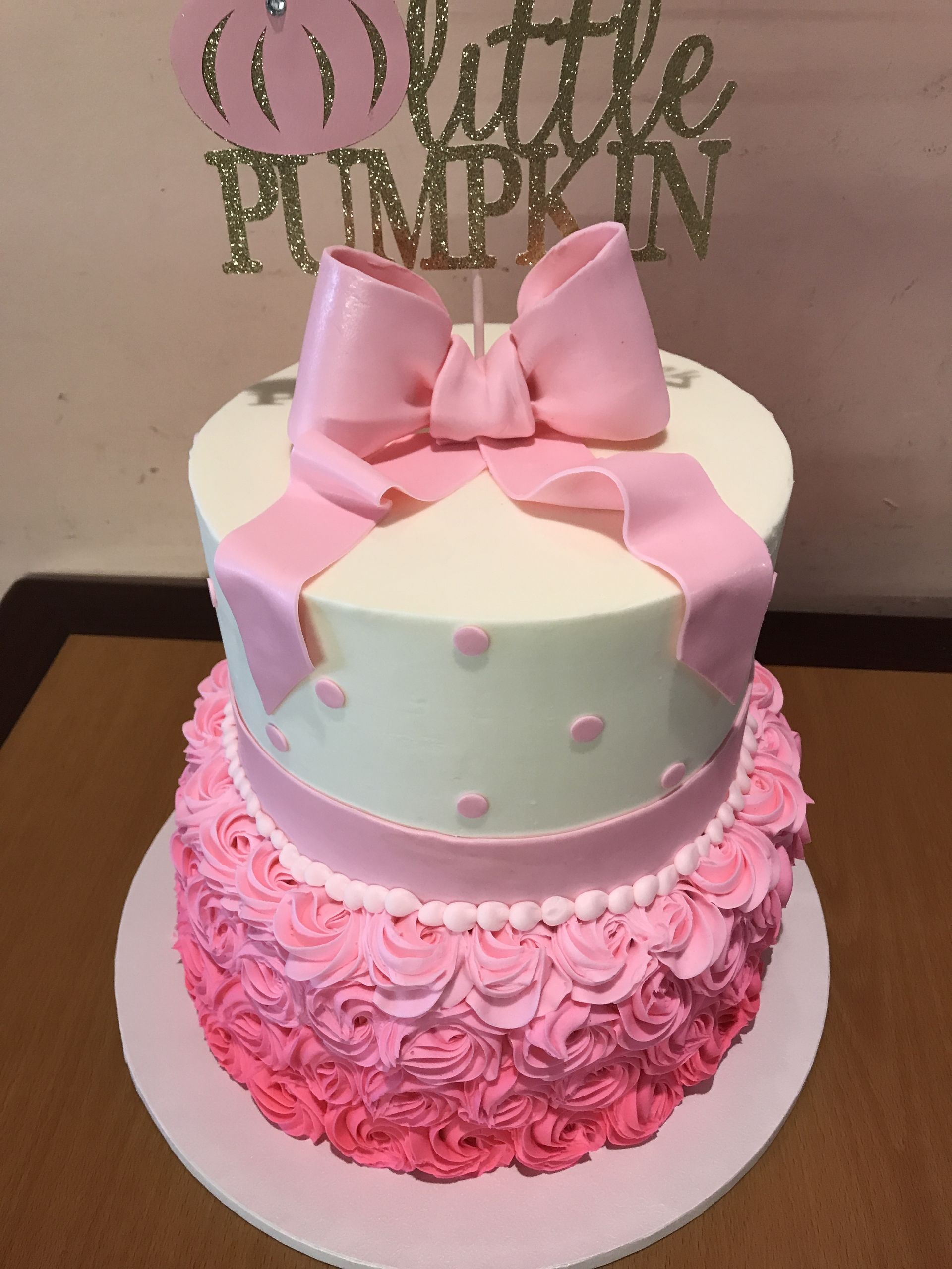 a pink and white cake with a little pumpkin topper