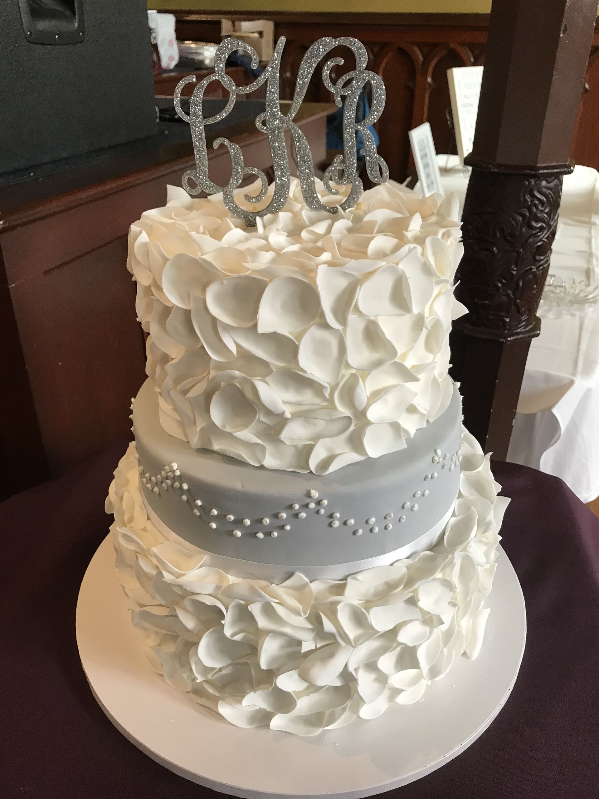 a white wedding cake with a silver monogram on top
