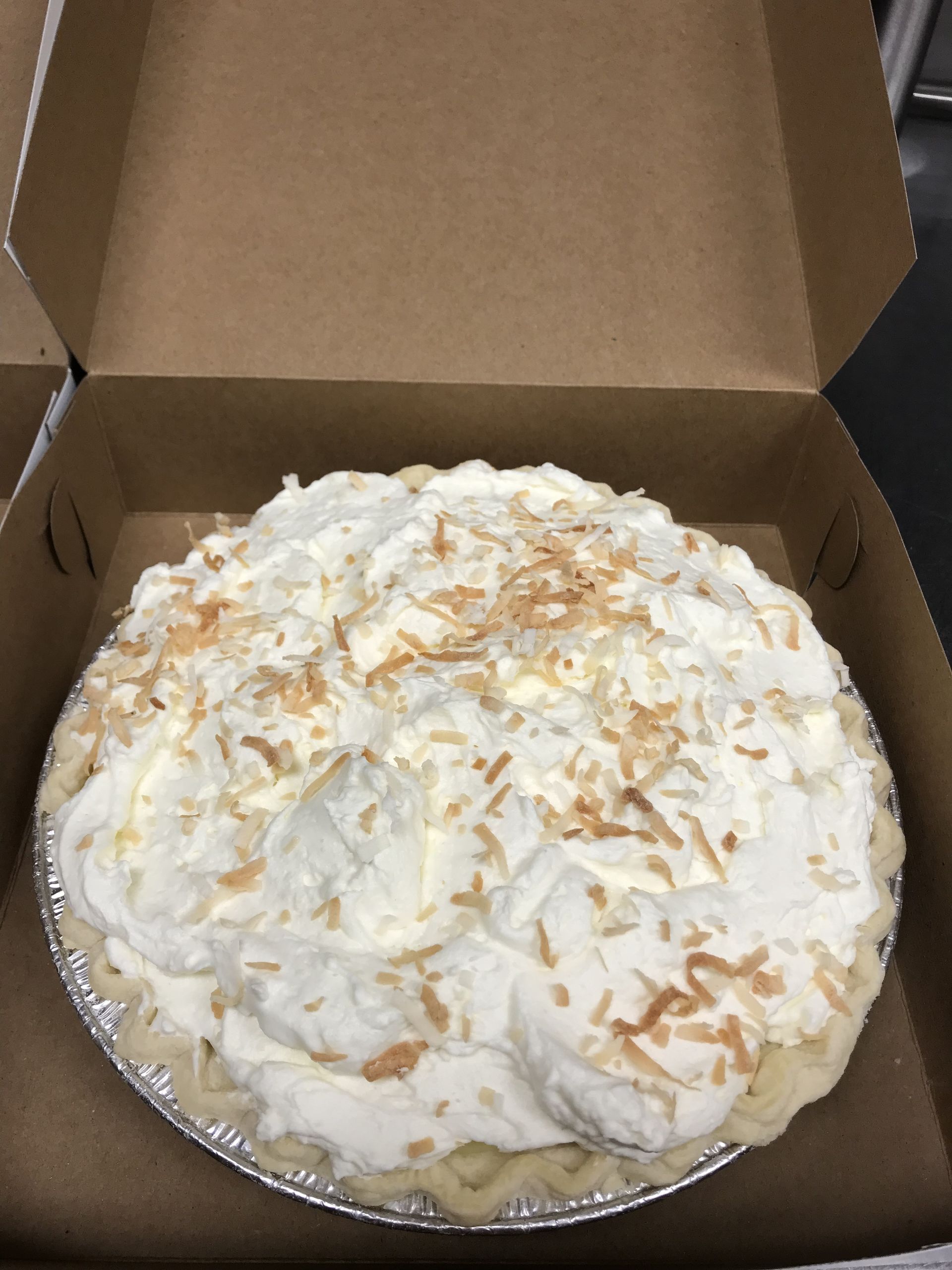 a coconut pie with whipped cream on top is in a cardboard box .