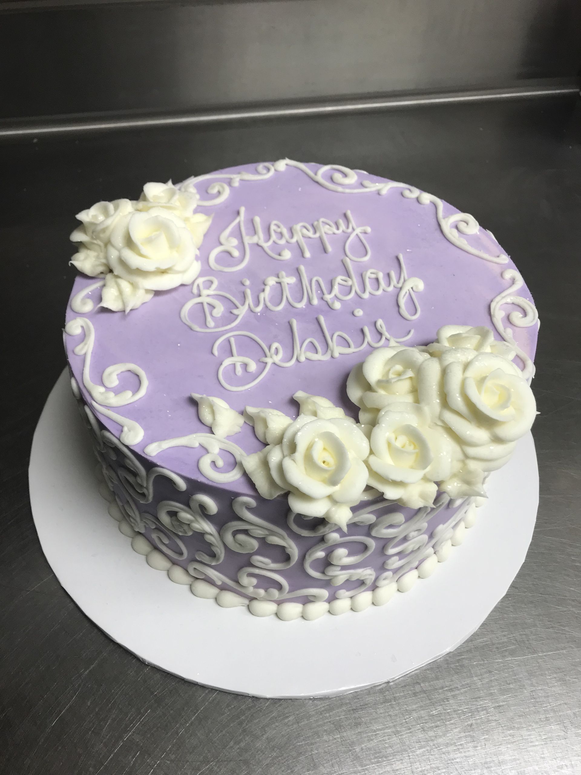 a purple birthday cake with white frosting and roses