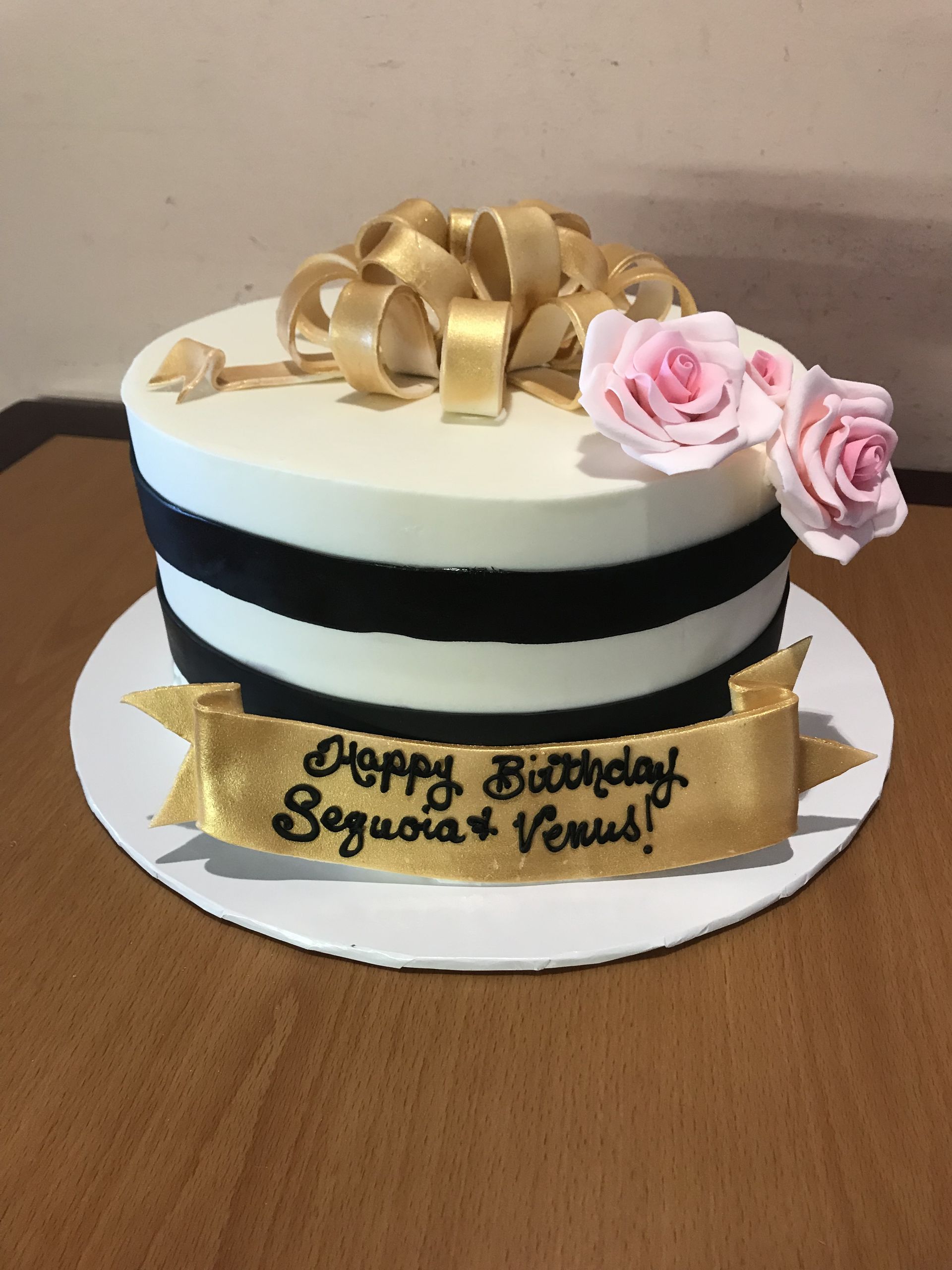a black and white birthday cake with pink roses and a gold bow