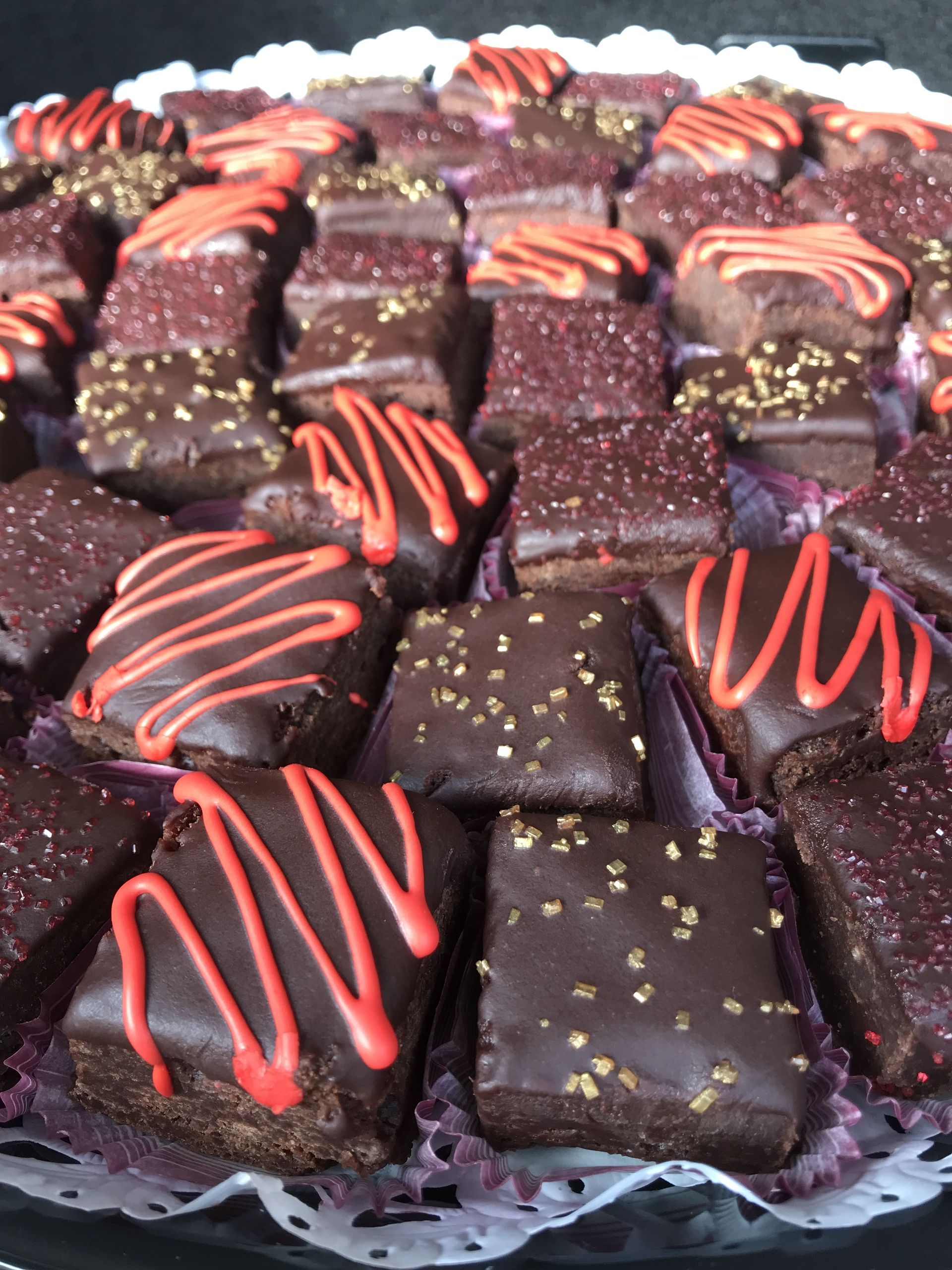 a tray of chocolate squares with red icing and gold sprinkles