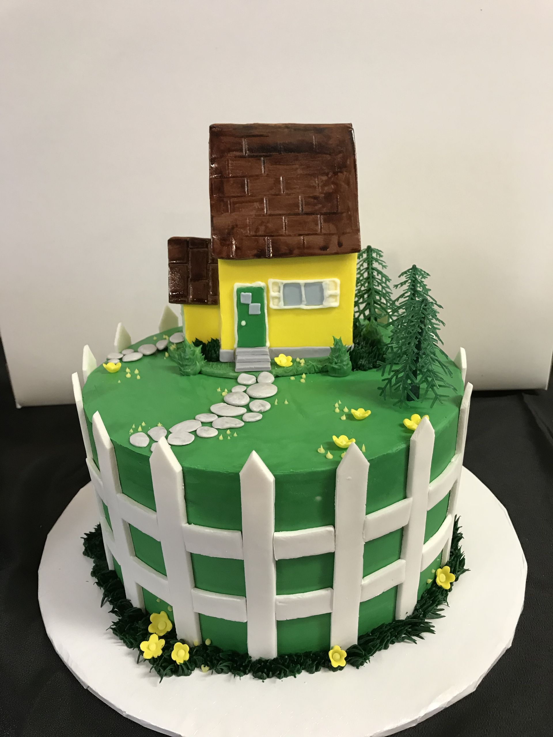 a cake with a yellow house and a white picket fence