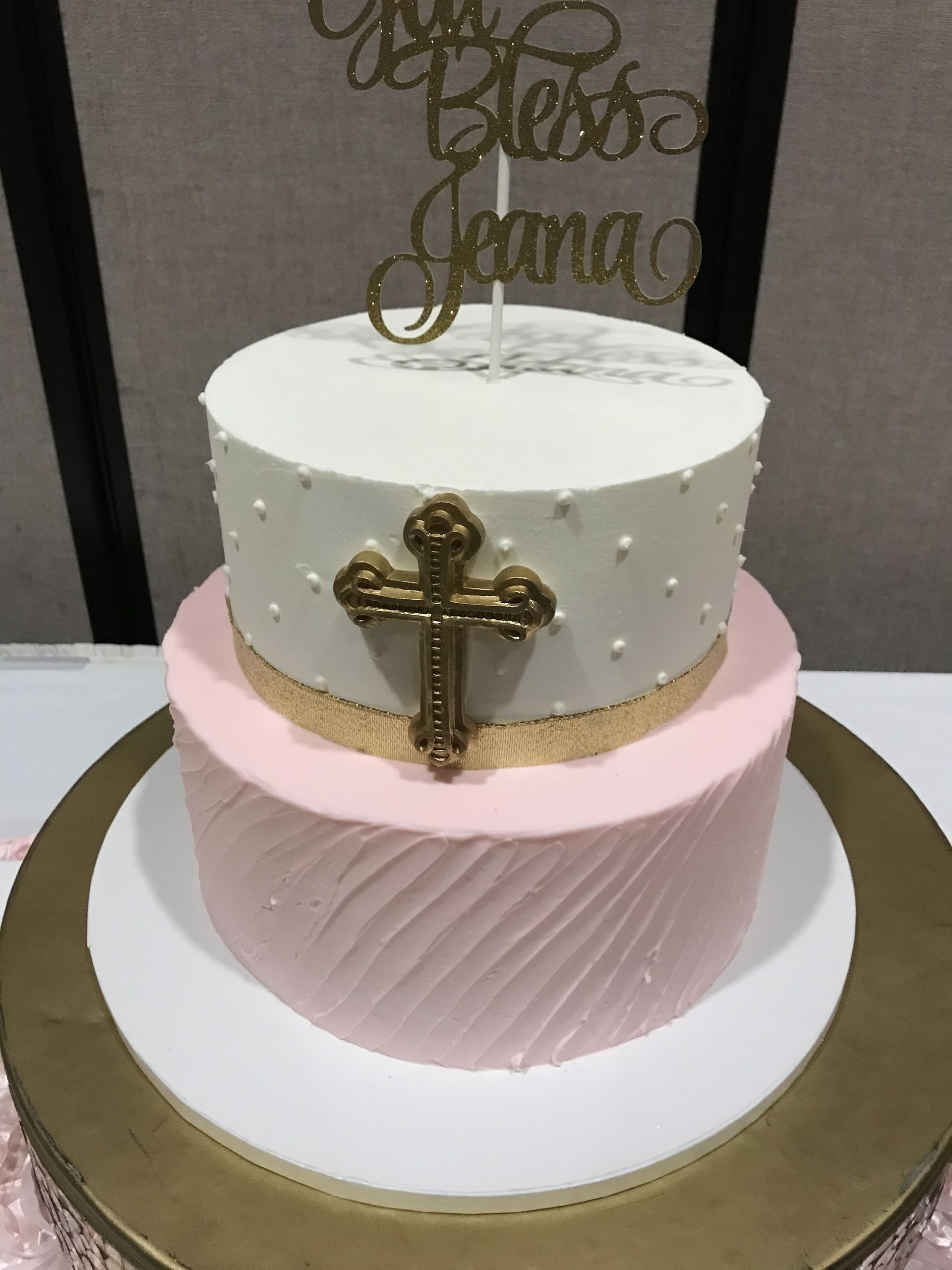 a pink and white cake with a gold cross on top