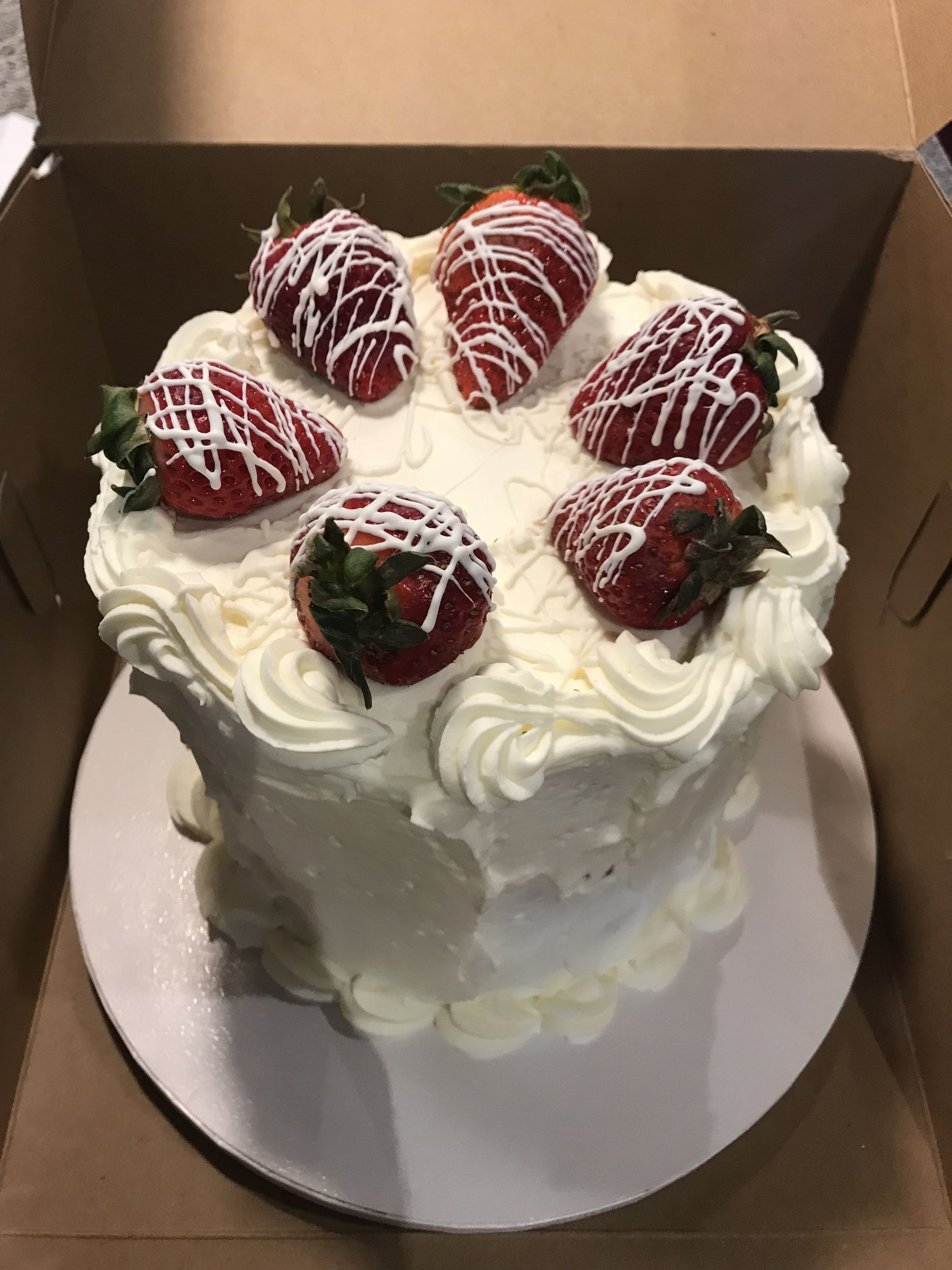 a white cake with strawberries on top is in a box .