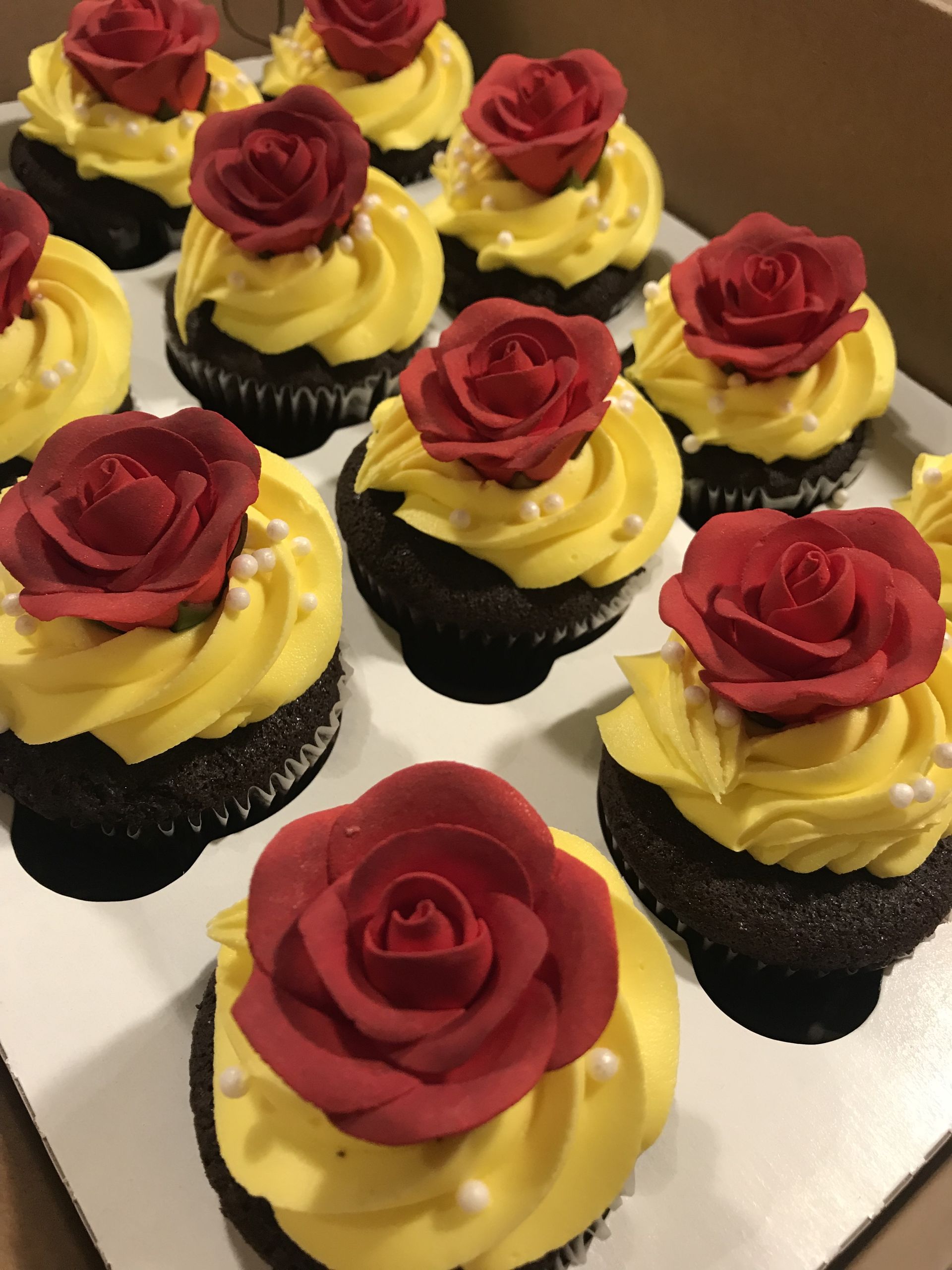 a box of cupcakes with yellow frosting and red roses