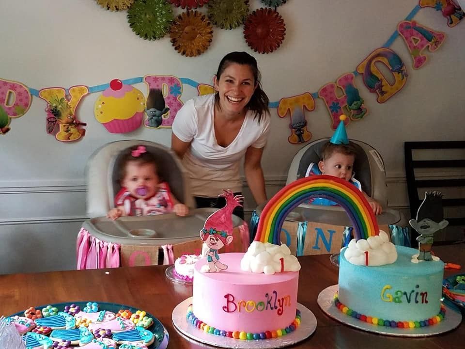 a woman stands next to two babies and a birthday cake with the name brooklyn on it