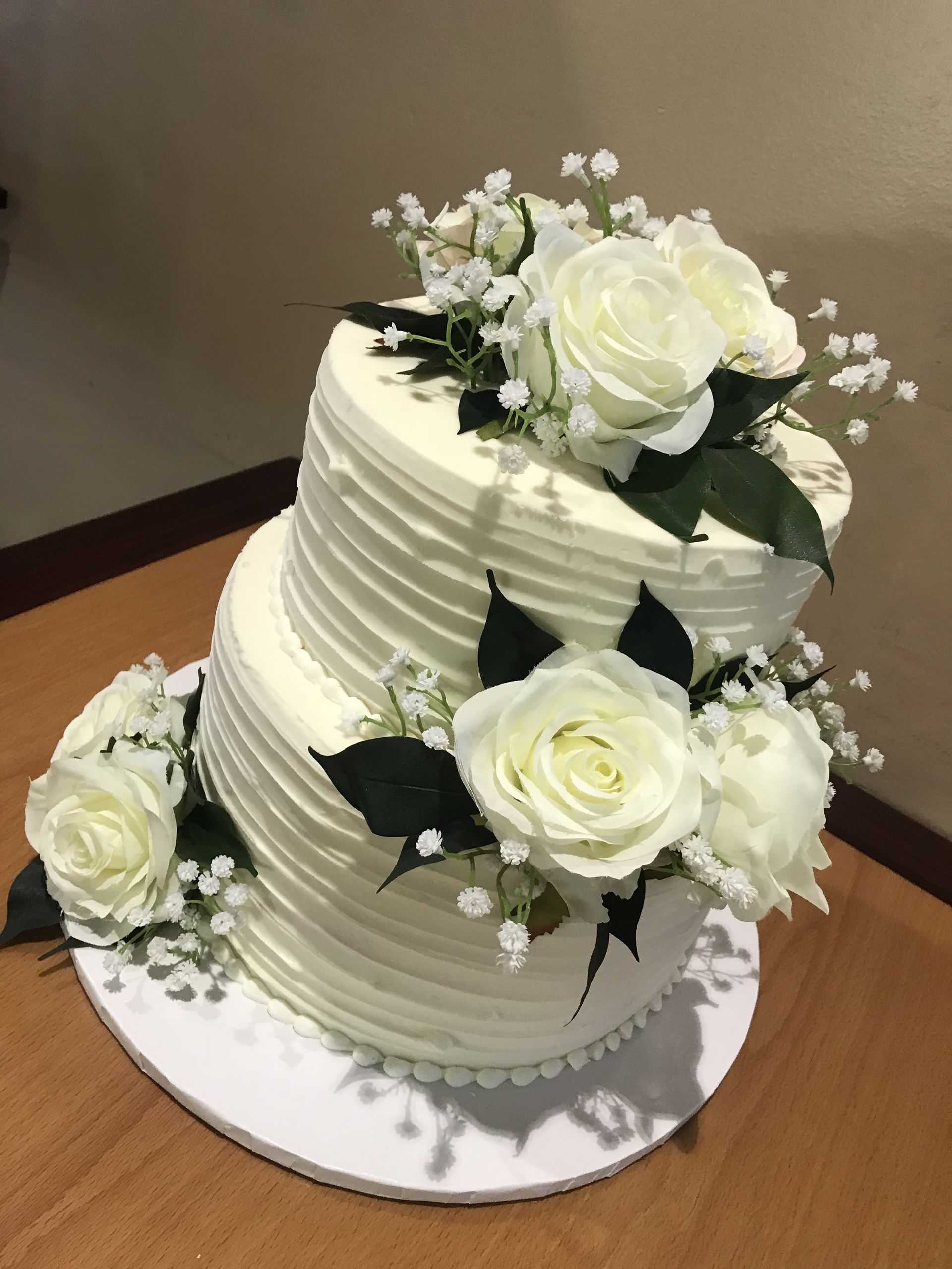 a white wedding cake with white roses and baby 's breath on a wooden table .