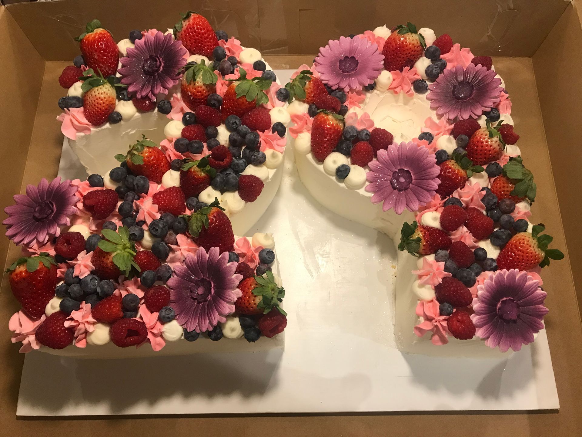 a cake in the shape of the number 20 decorated with berries and flowers