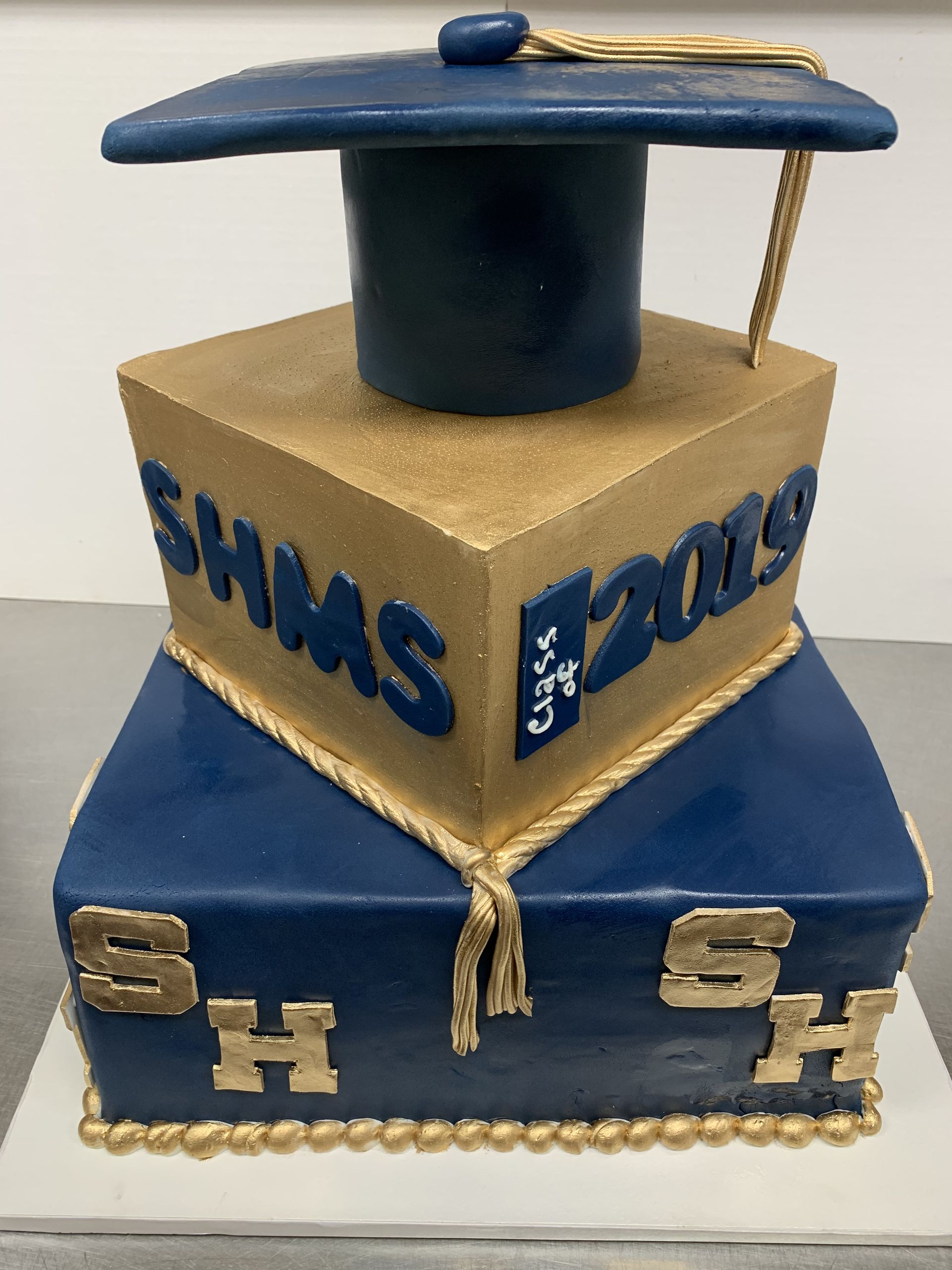 a blue and gold cake with a graduation cap on top