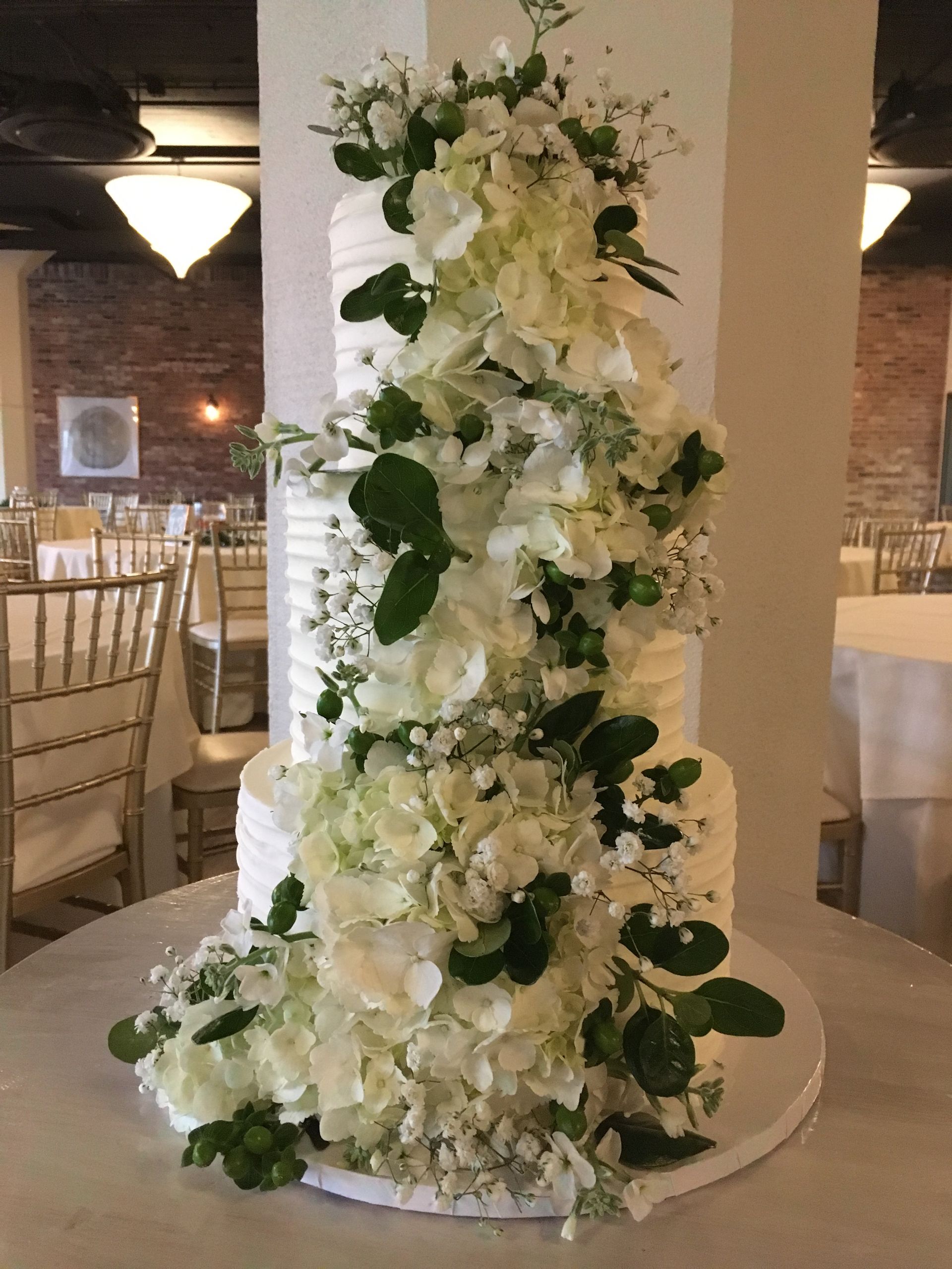 a wedding cake with white flowers and green leaves is sitting on a table .