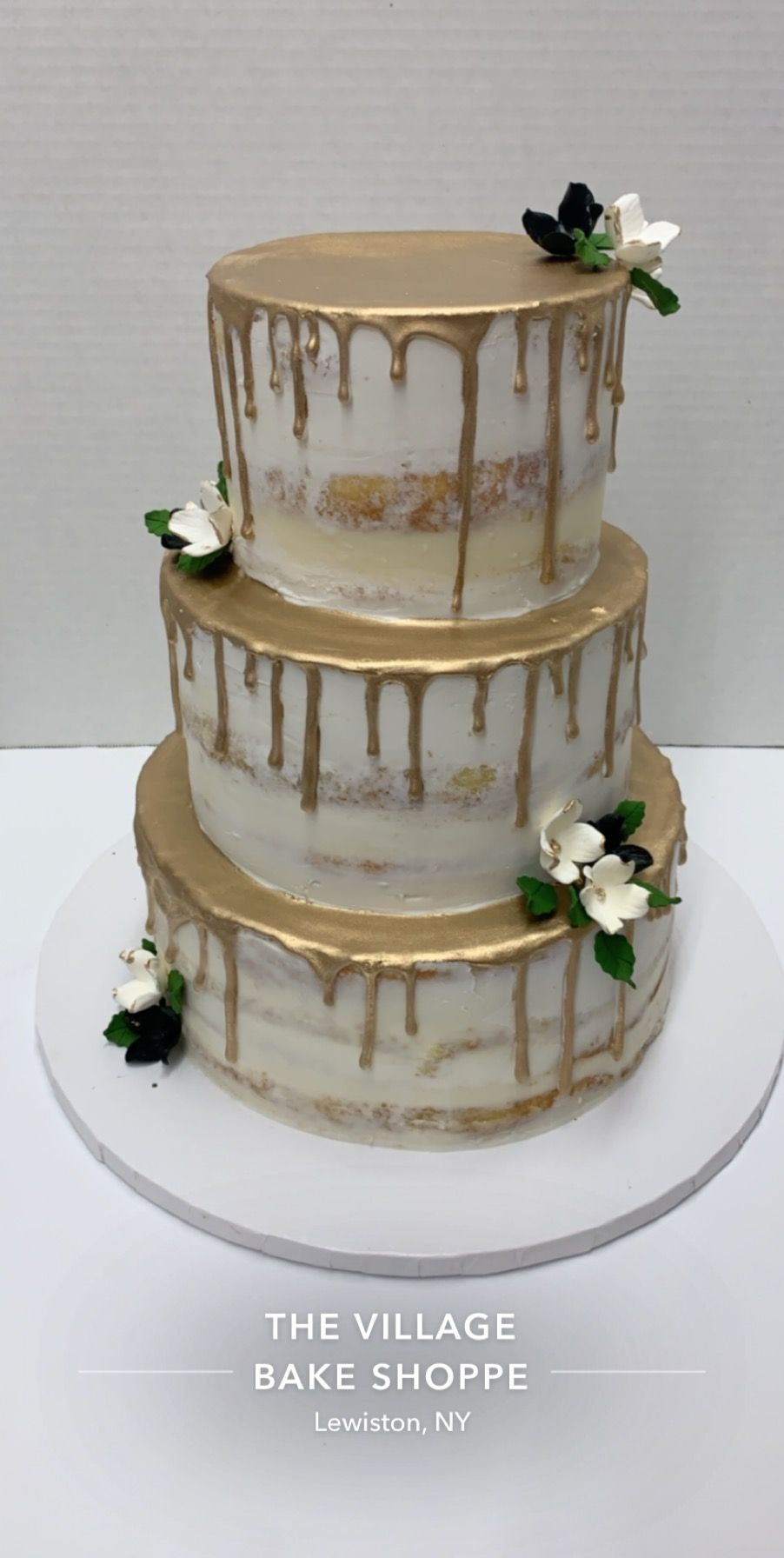 a three tiered cake with gold frosting and flowers on a white plate .