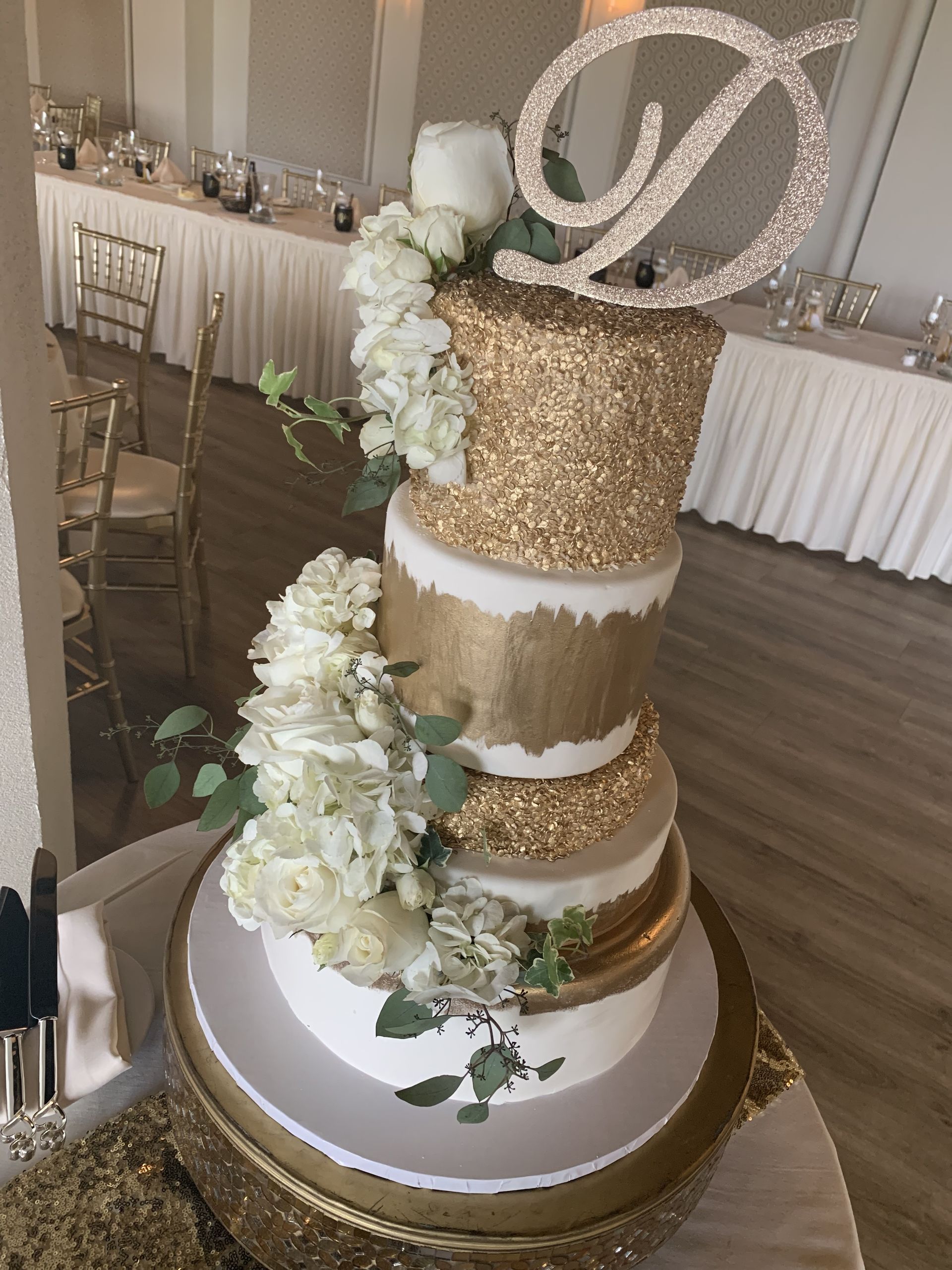 a wedding cake with flowers and a letter d on top is sitting on a table .