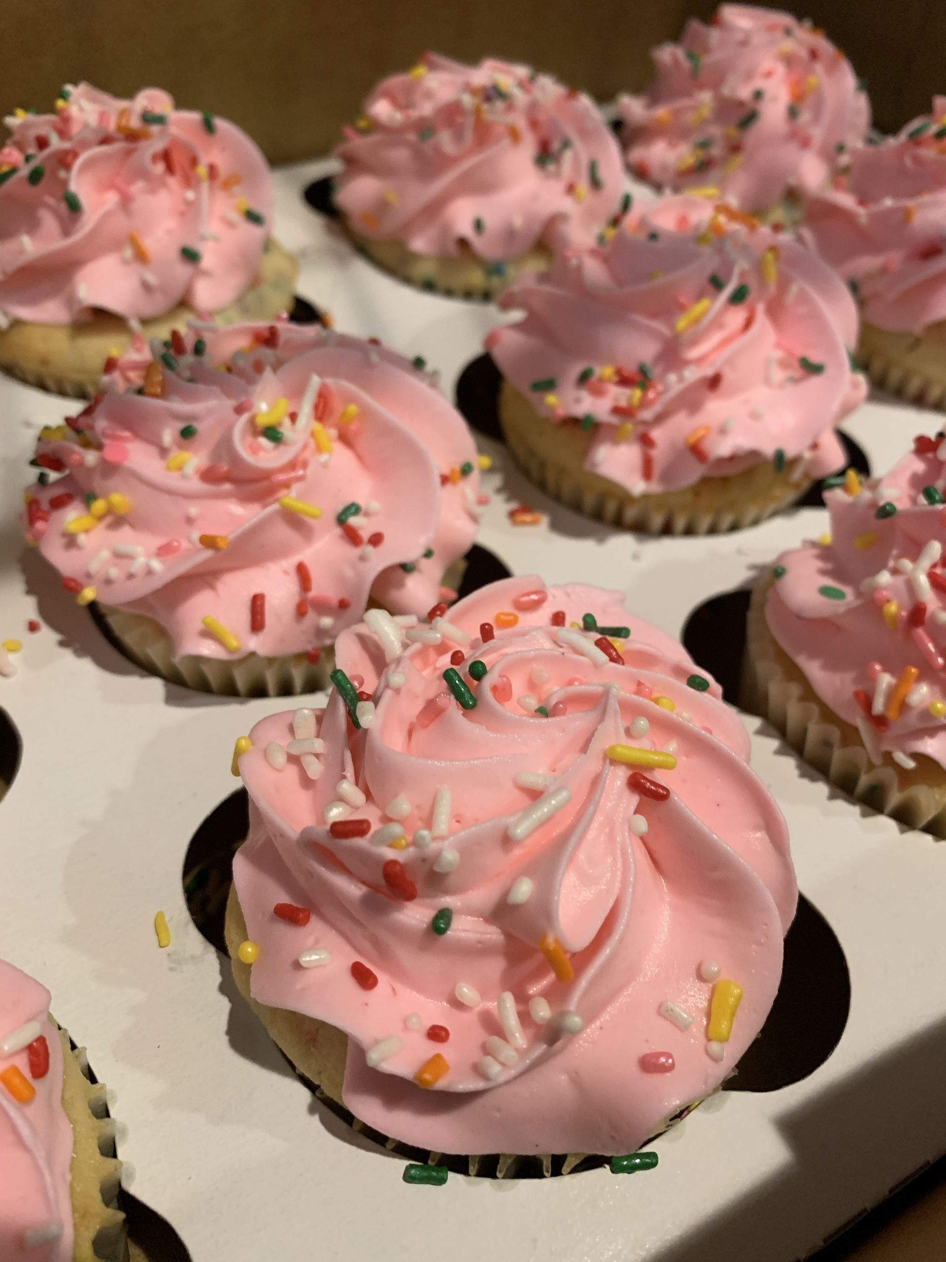 a box of cupcakes with pink frosting and sprinkles
