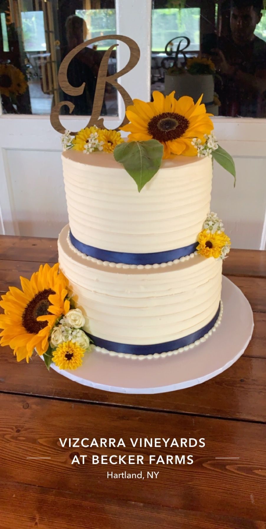 a wedding cake with sunflowers and a blue ribbon on a wooden table .