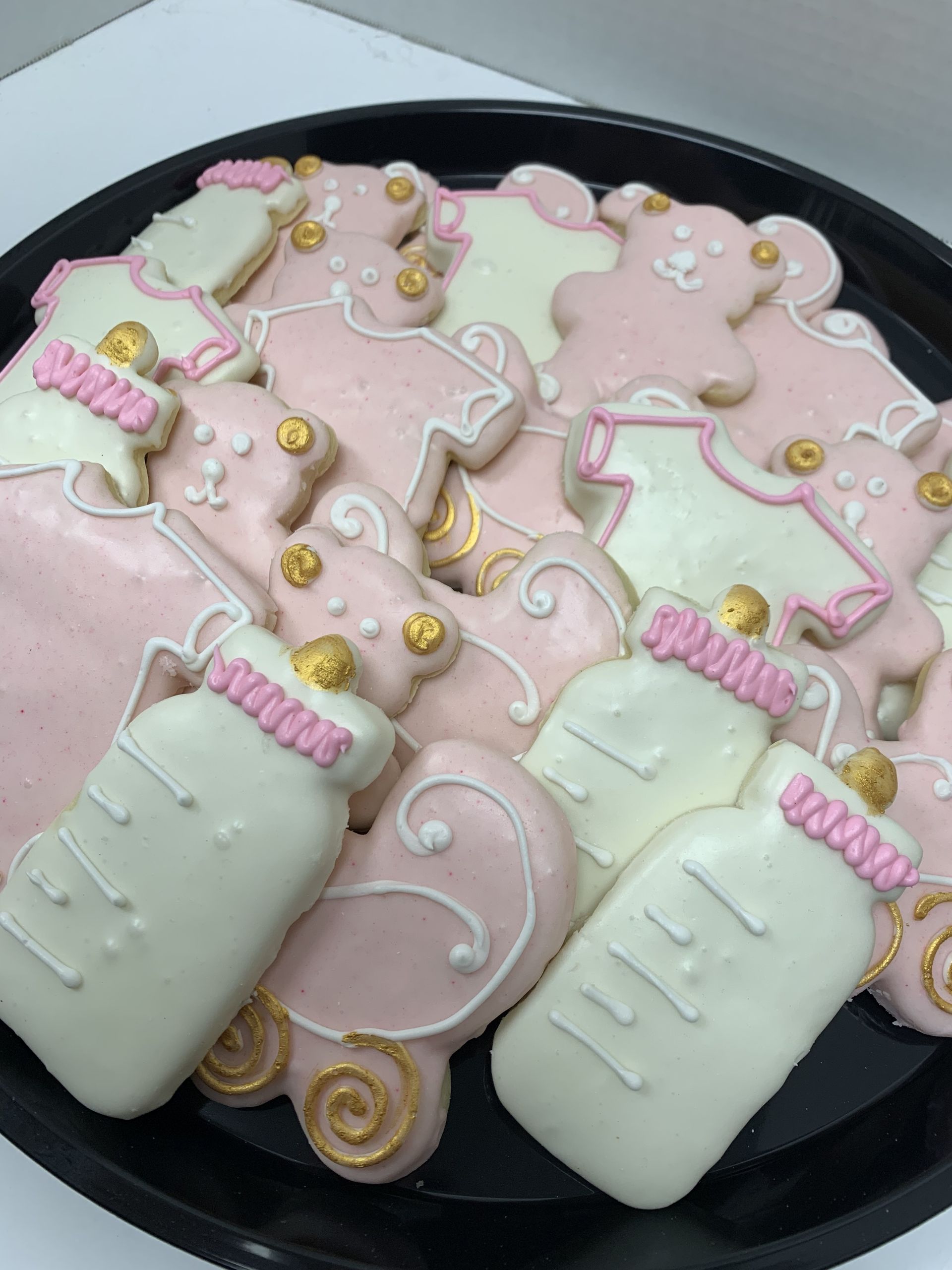 a black plate topped with pink and white cookies in the shape of baby bottles