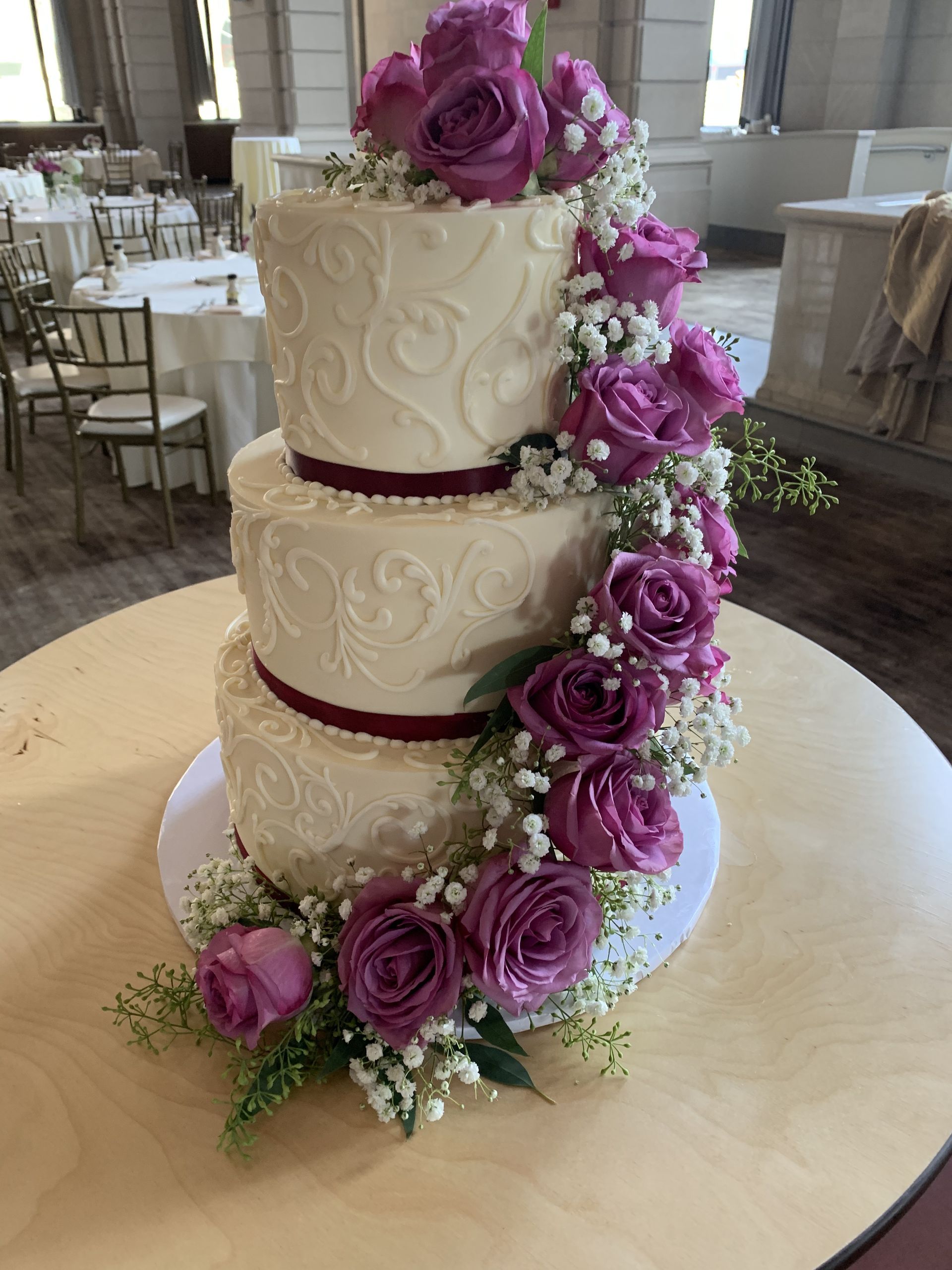a wedding cake with purple roses and baby 's breath on a table .