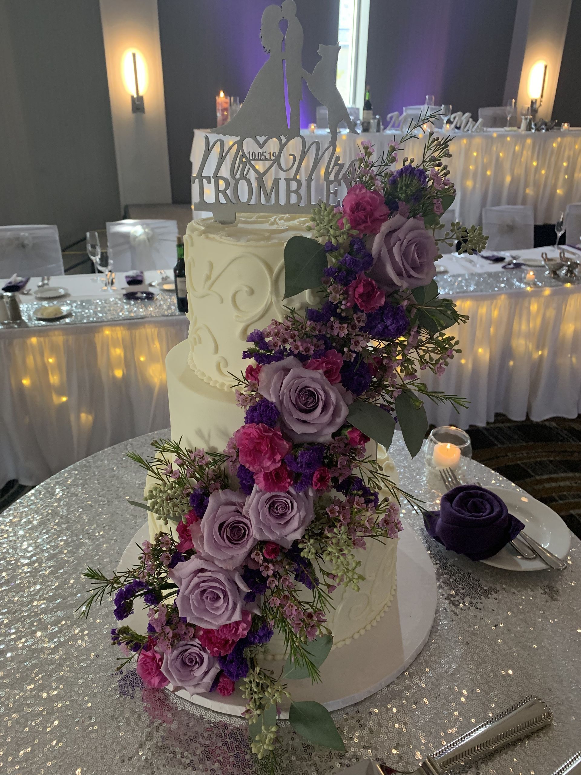 a wedding cake with purple and pink flowers is on a table .
