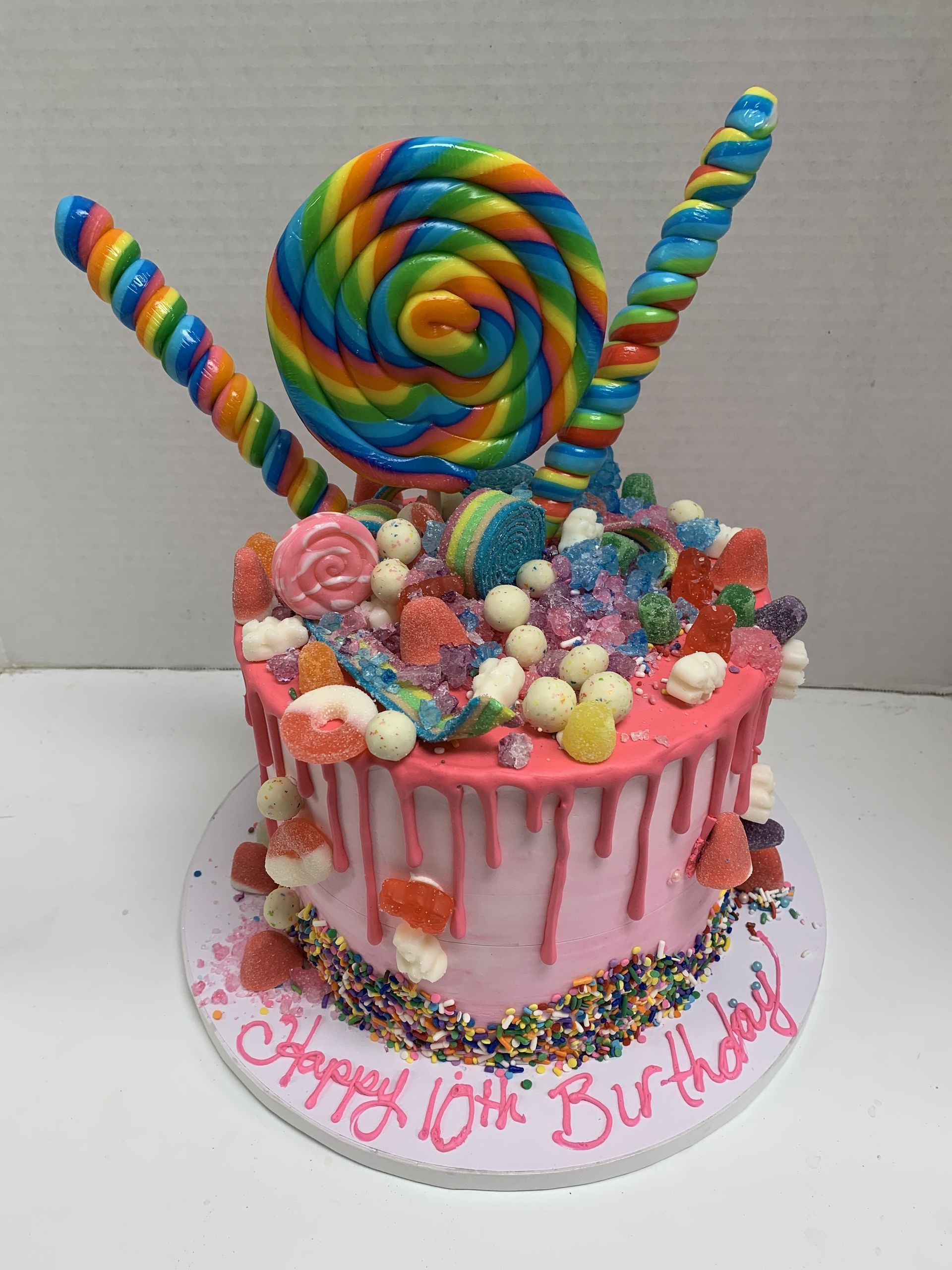 a pink birthday cake with candy and lollipops on top