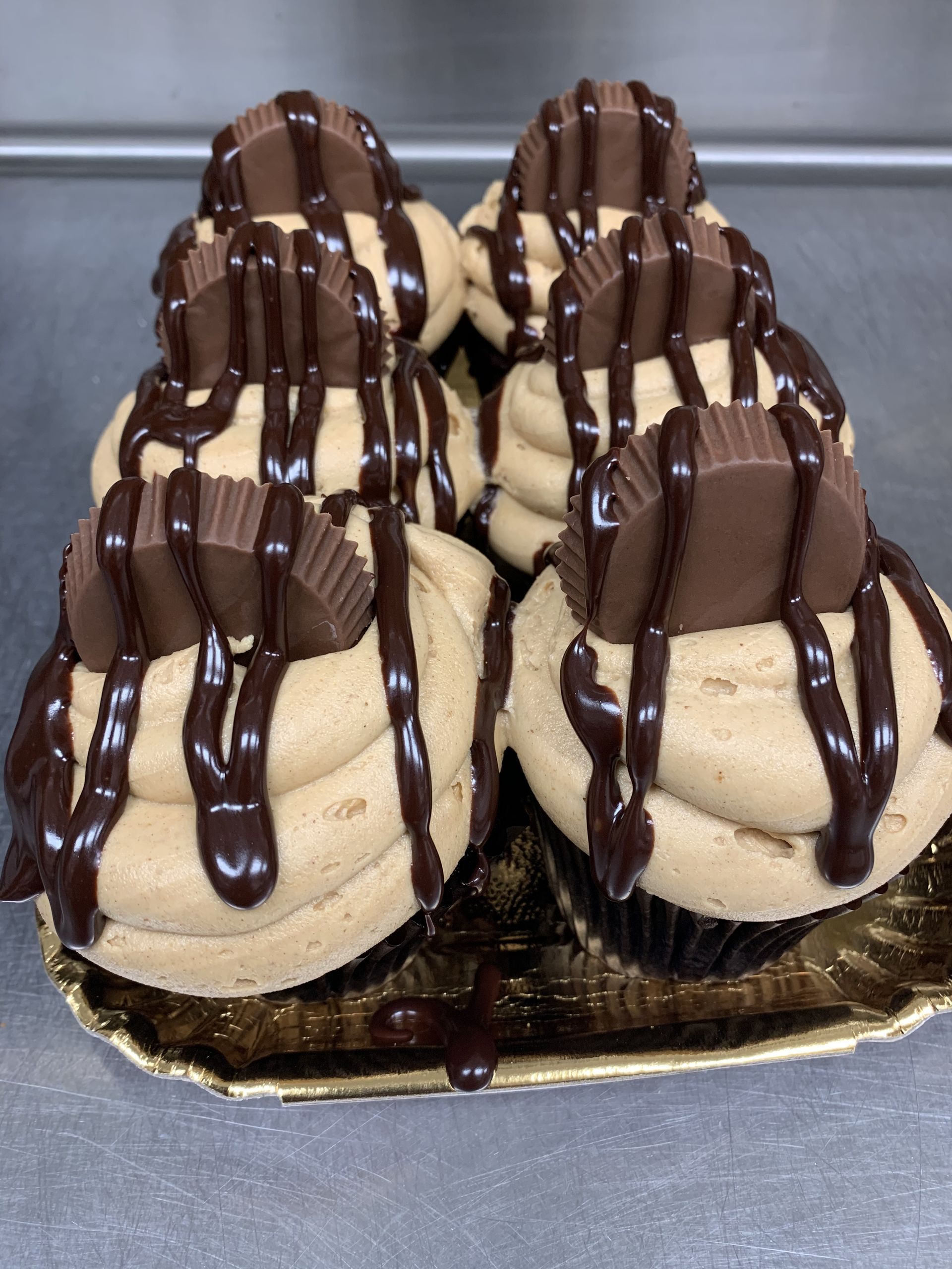 four cupcakes with peanut butter frosting and chocolate drizzle on a tray .