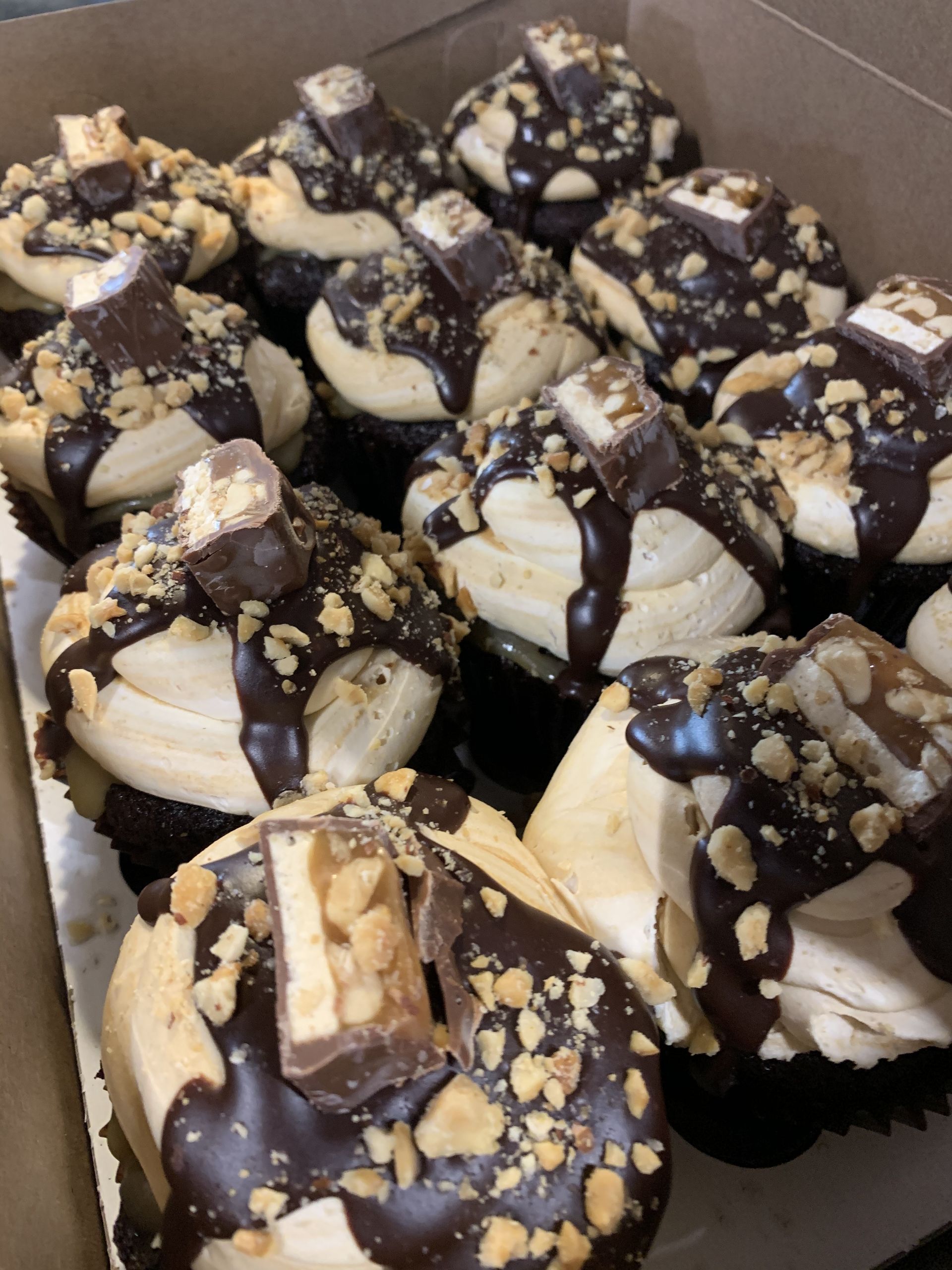 a box of cupcakes with chocolate frosting and nuts on top