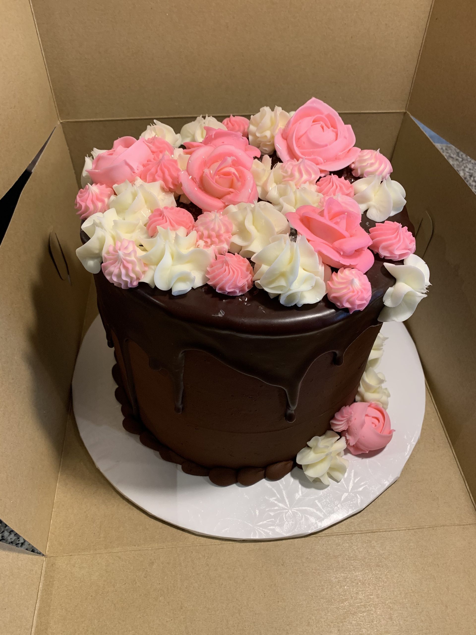 a chocolate cake with pink and white frosting is in a box .