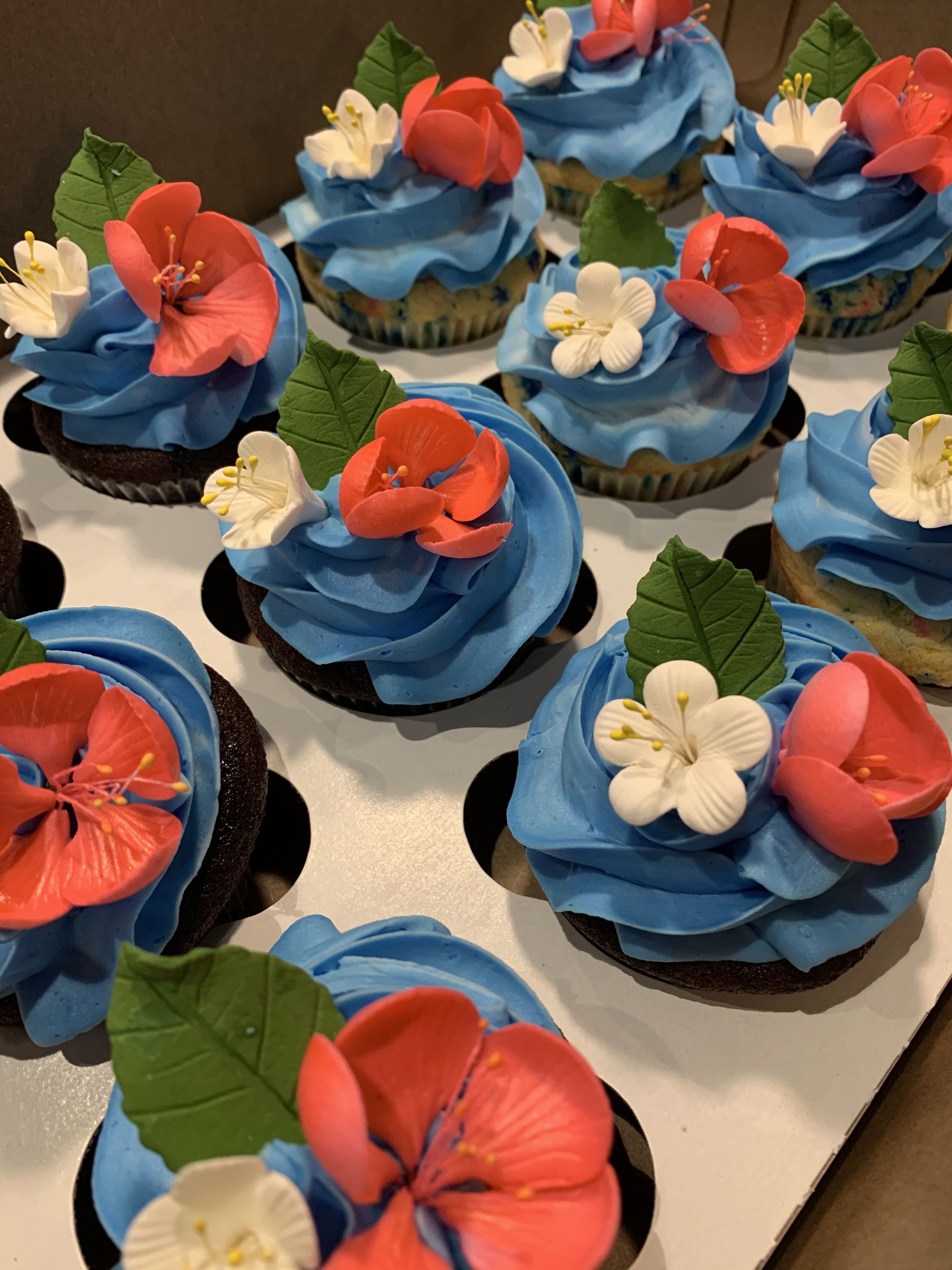a bunch of cupcakes with blue frosting and flowers on them