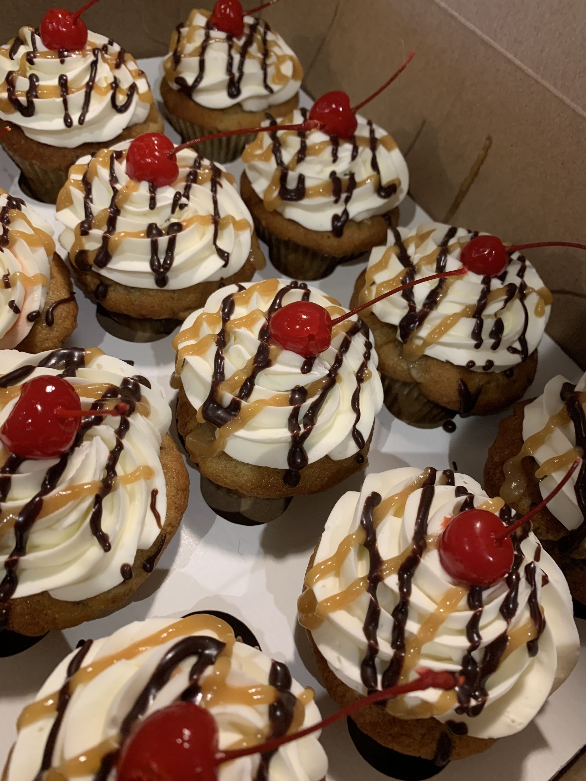 a box of cupcakes with whipped cream and cherries on top