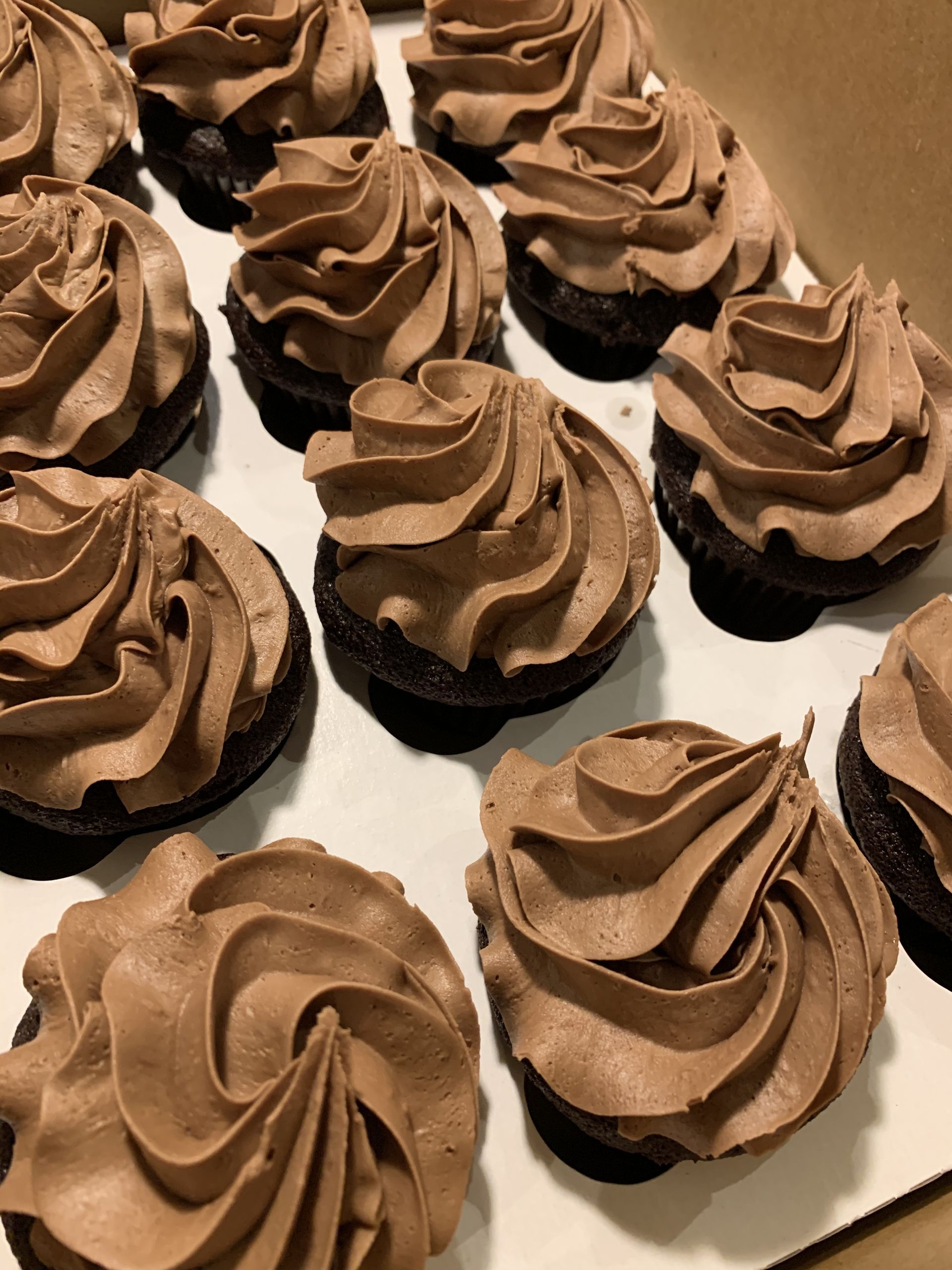 a box of chocolate frosted cupcakes on a table .