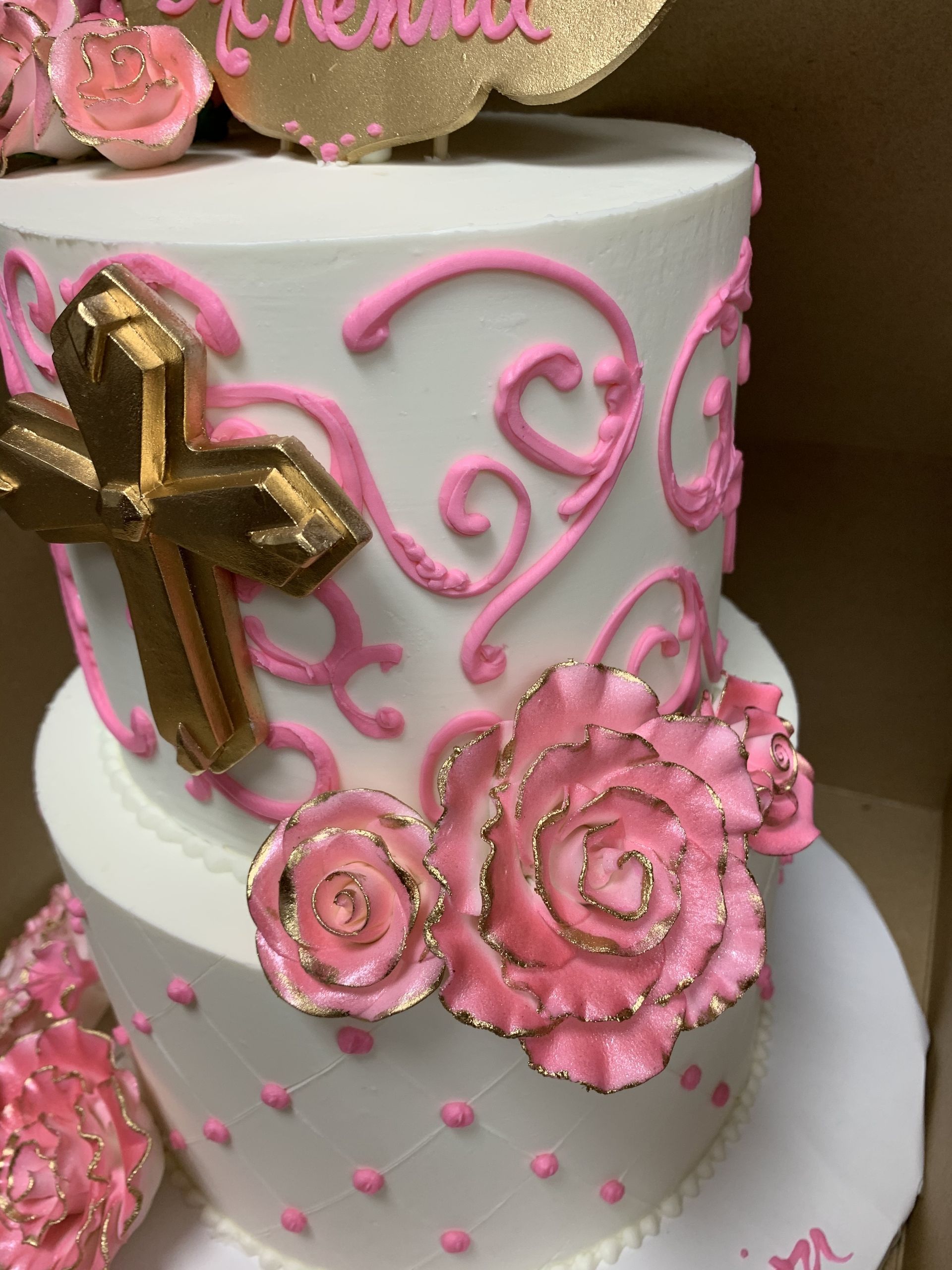 a white cake with pink roses and a gold cross on top