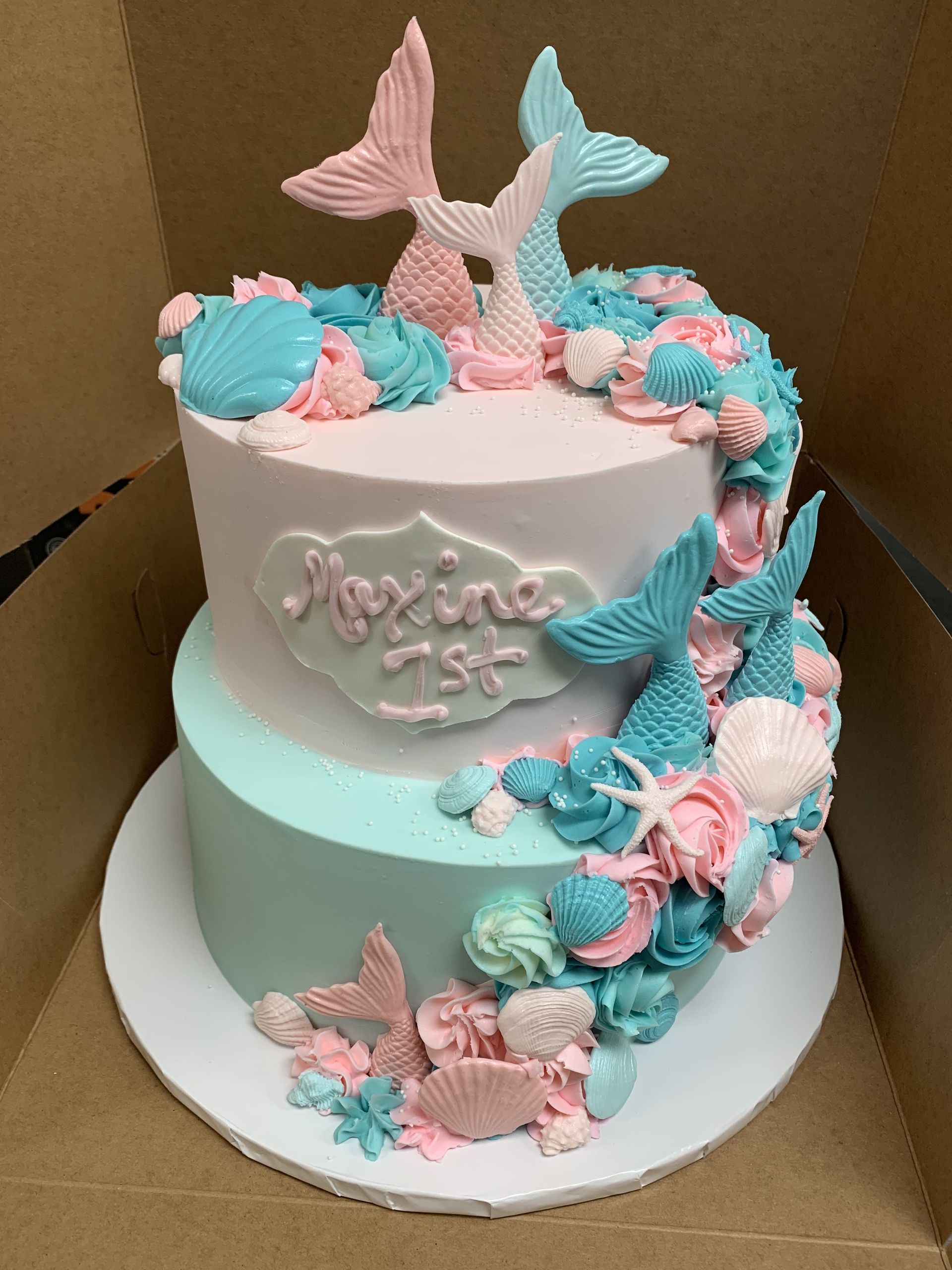 a cake decorated with mermaid tails and seashells is in a box .