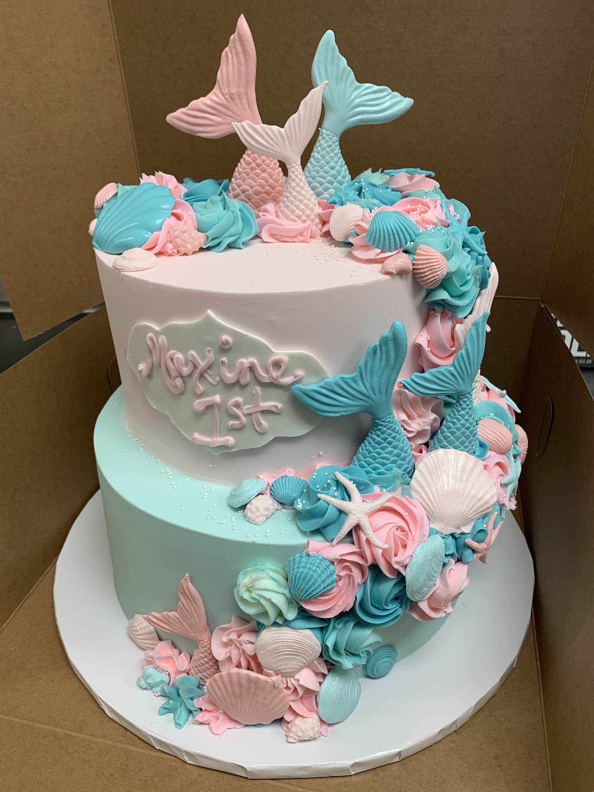 a cake with mermaids and seashells on it is in a box .